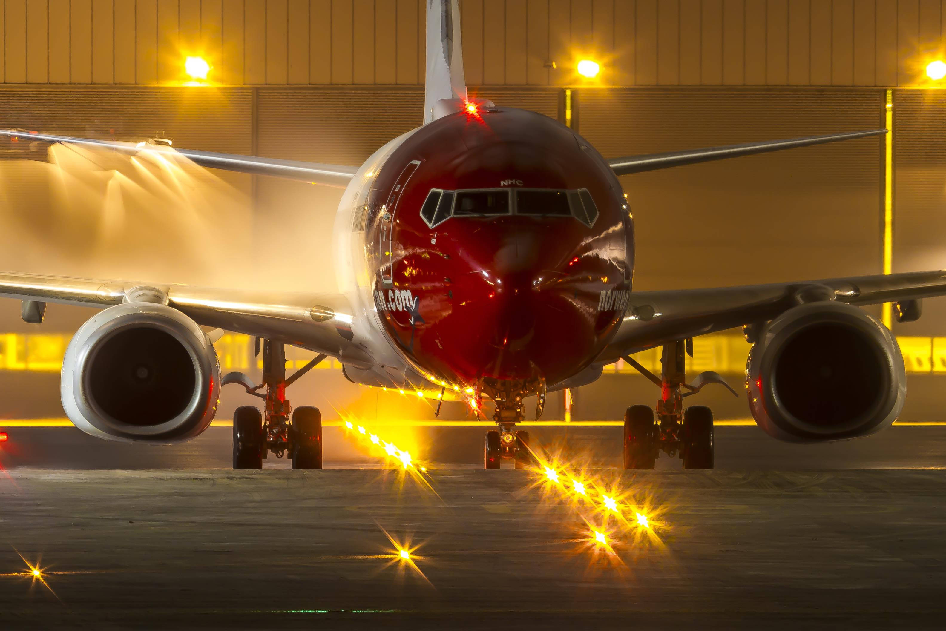 Airport 桌布 壁紙 — 一架紅色飛機在夜間正面拍攝，跑道上有發光的黃色燈光，停機坪上蒸氣升騰。