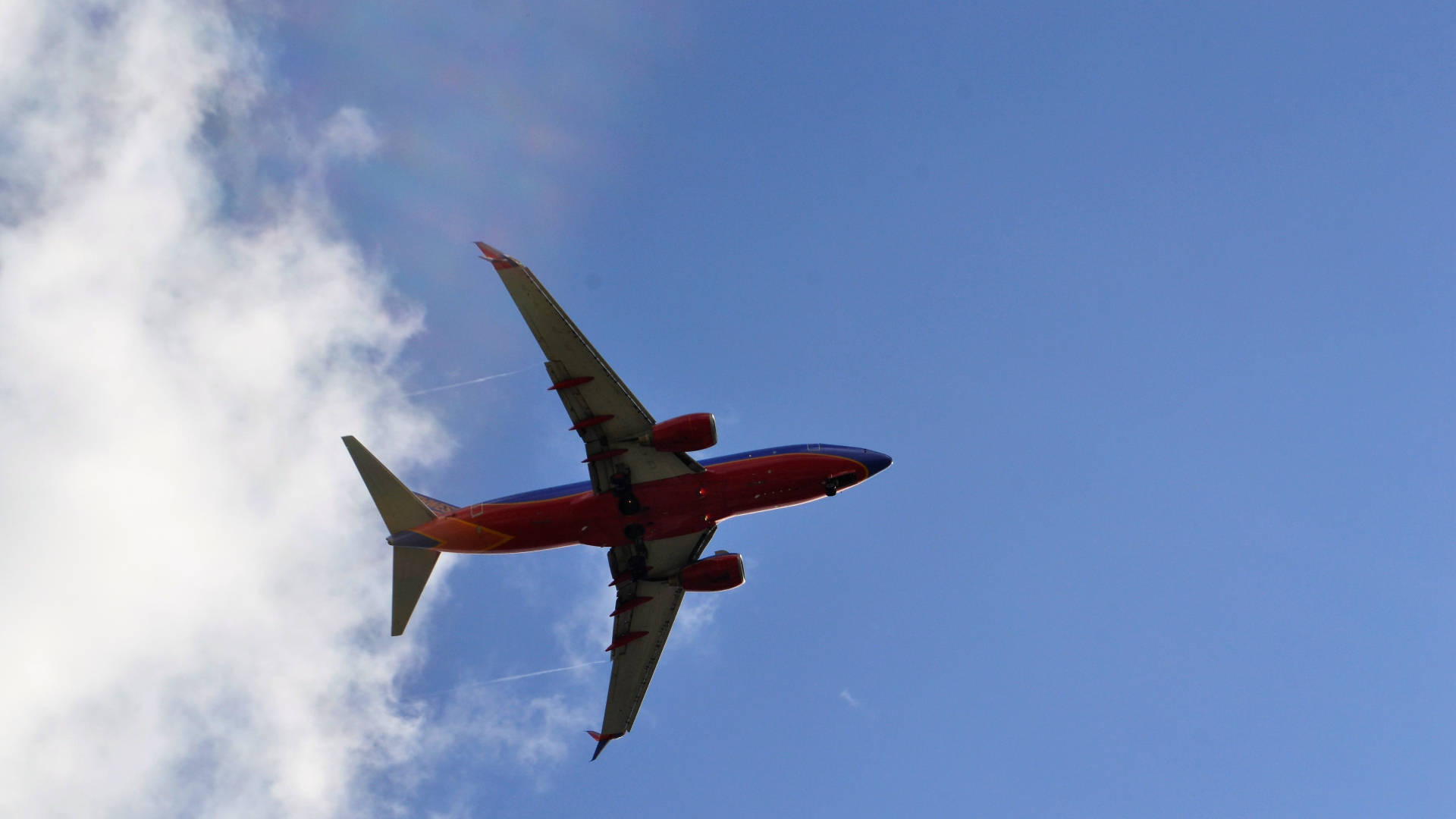 飛機 桌布 壁紙 — 一架紅藍相間的西南航空飛機在晴朗的藍天中翱翔，伴隨著蓬鬆的白雲。