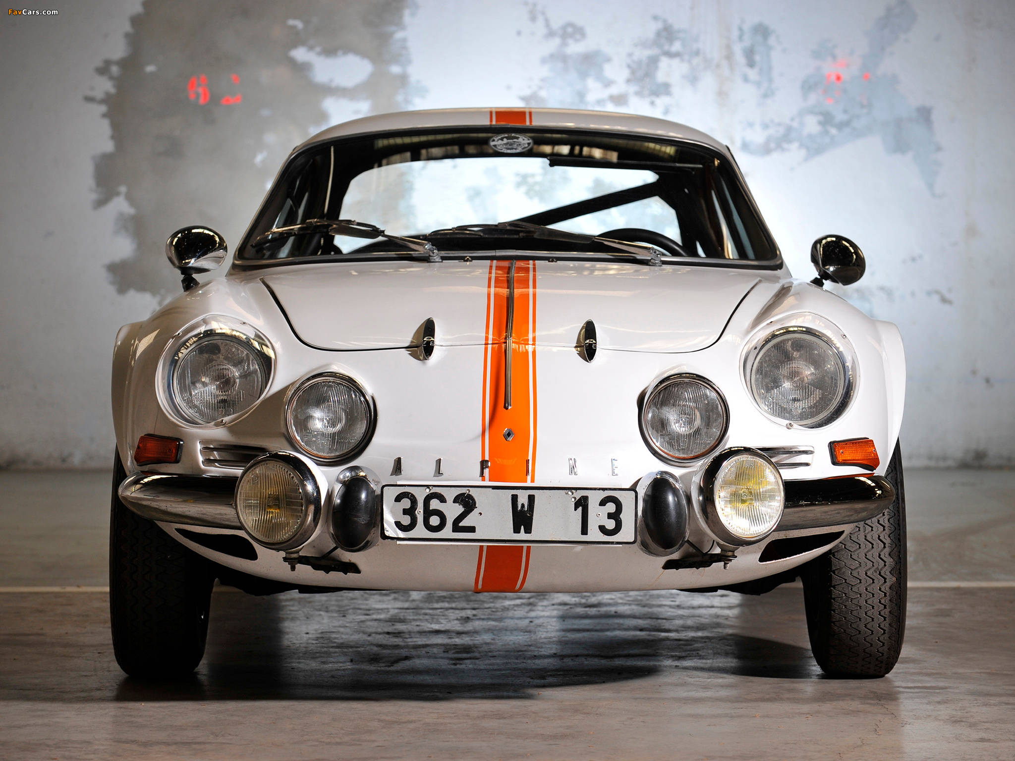 復古 桌布 壁紙 — 一架純白色的Alpine A110賽車，帶有醒目的橙色條紋和四個頭燈，在骯髒的車庫中直視前方。