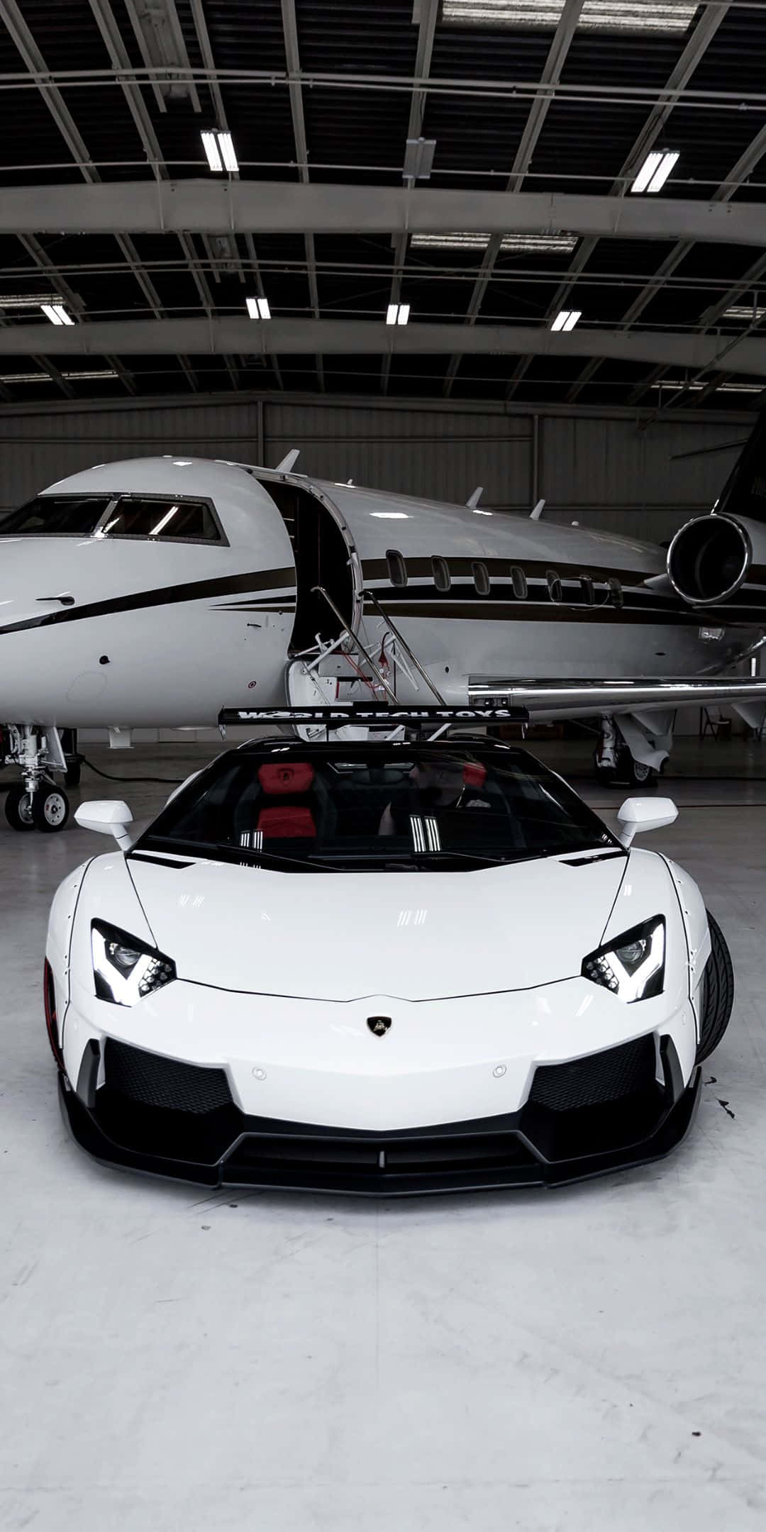 Pixel 3 Lamborghini 桌布 壁紙 — 一架純白色的藍寶堅尼 Aventador 停放在機庫內，旁邊是一架艙門打開的私人飛機。