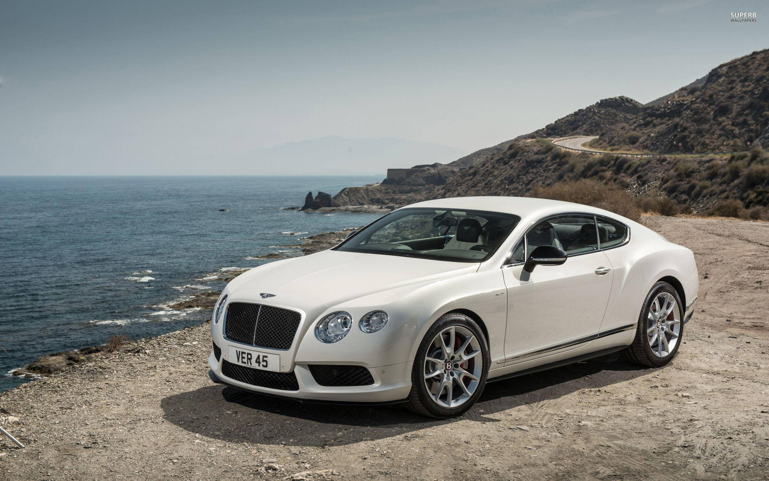 賓利 桌布 壁紙 — 一架純白色的賓利 Continental GT 雙門跑車停泊在崎嶇的海岸懸崖上，俯瞰深藍色的大海。