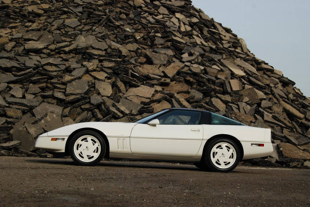 corvette 桌布 壁紙 — 一架純白色經典Corvette跑車停泊在陰天下高聳的粗糙板岩堆前。