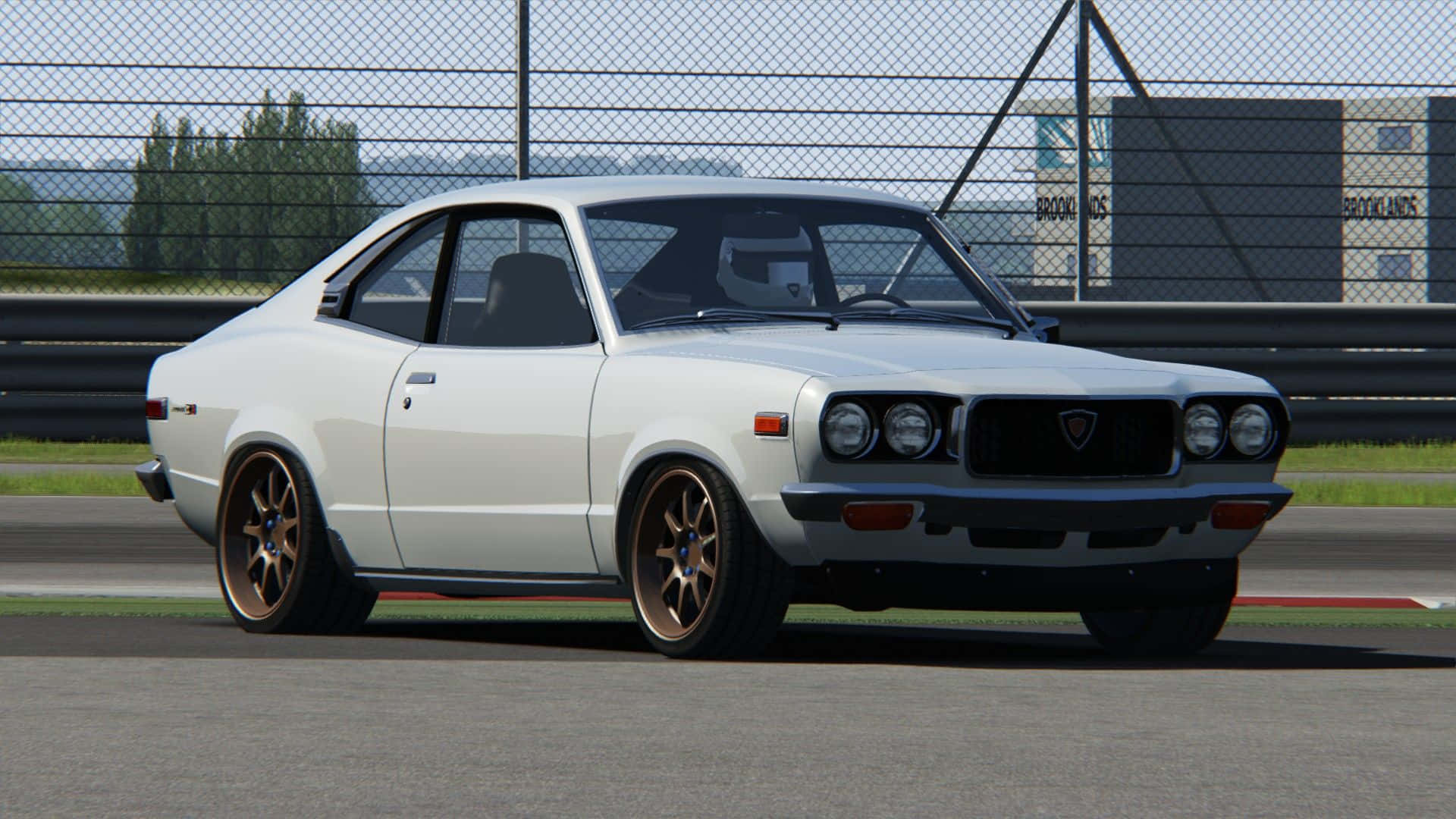 Mazda Rx-3 桌布 壁紙 — 一架純白色經典賽車配青銅輪圈，在晴朗日光下停泊在賽道上。