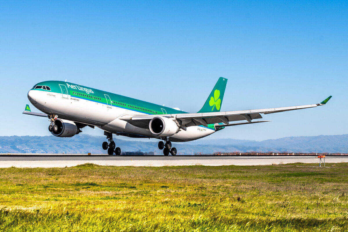 飛機 桌布 壁紙 — 一架綠色和白色的愛爾蘭航空空中巴士A330在草地前景和遠處山丘的背景下，於晴朗藍天下從跑道起飛。