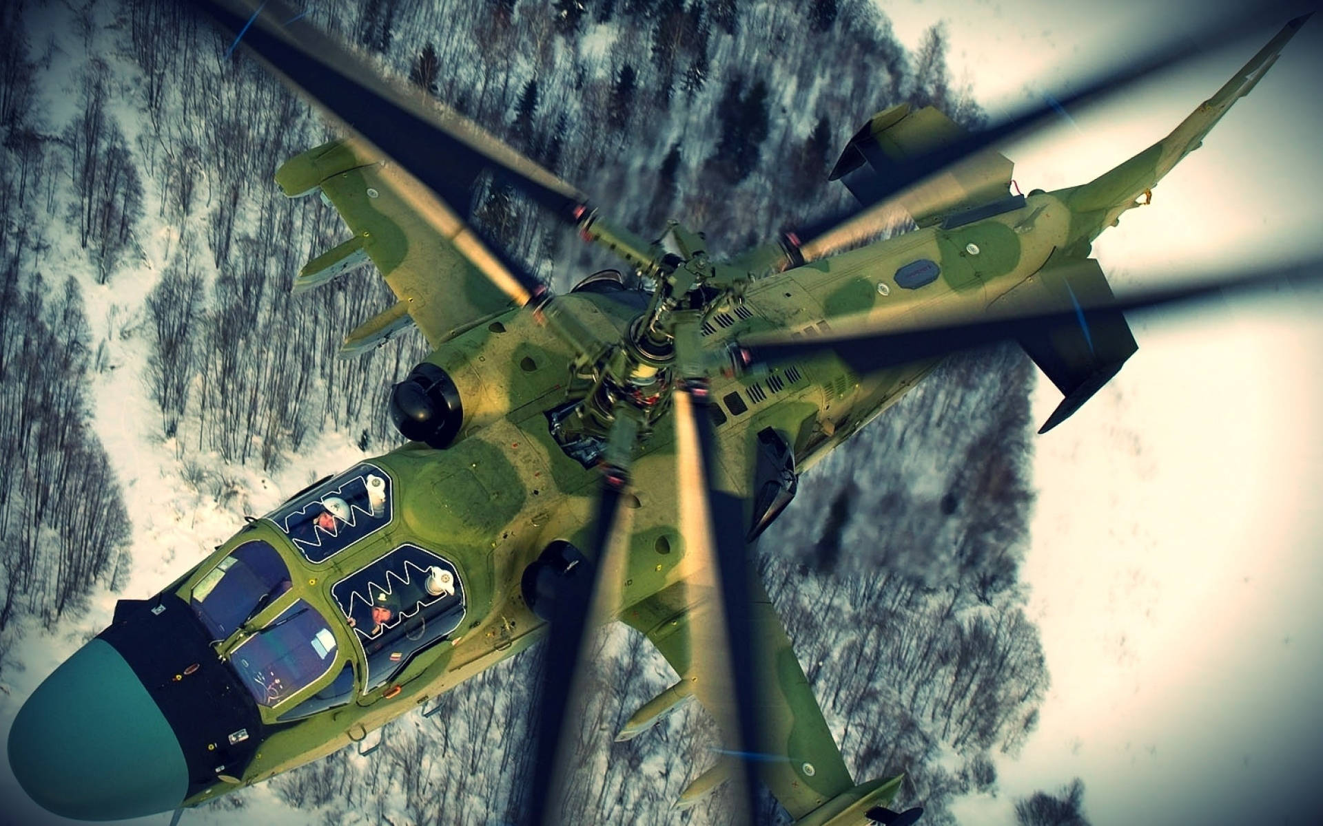 Helicopter 桌布 壁紙 — 一架綠色迷彩軍用直升機低飛過雪覆蓋的森林，前景有旋轉的槳葉。