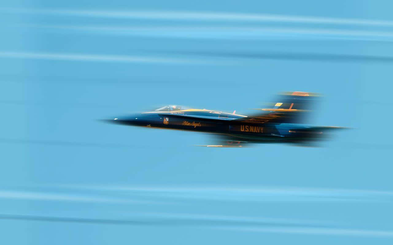 US Navy 桌布 壁紙 — 一架美國海軍藍天使特技飛行隊的噴射機，在清澈的藍天中高速飛行，動態模糊效果強調其高速飛行。