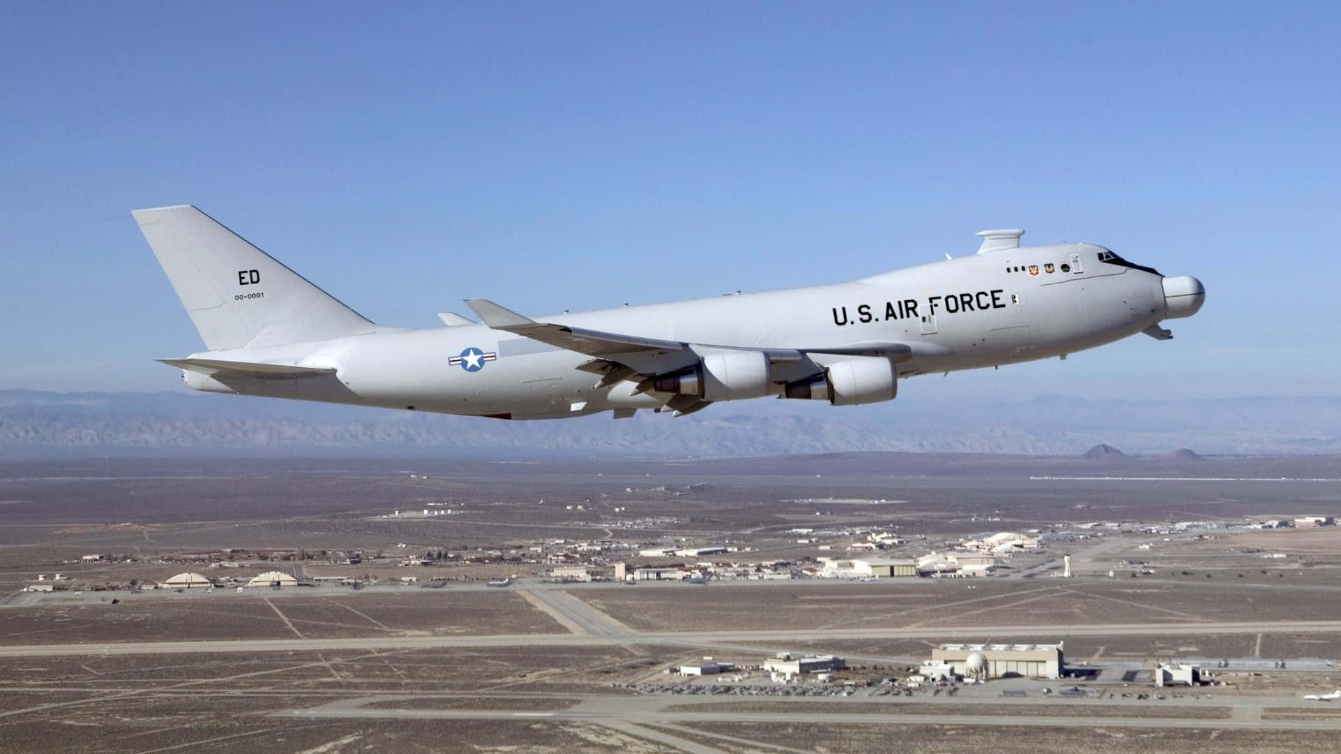 1920x1080 Jumbo Jets 桌布 壁紙 — 一架美國空軍KC-135同溫層加油機在晴朗藍天下，飛越沙漠空軍基地，遠方山巒起伏。
