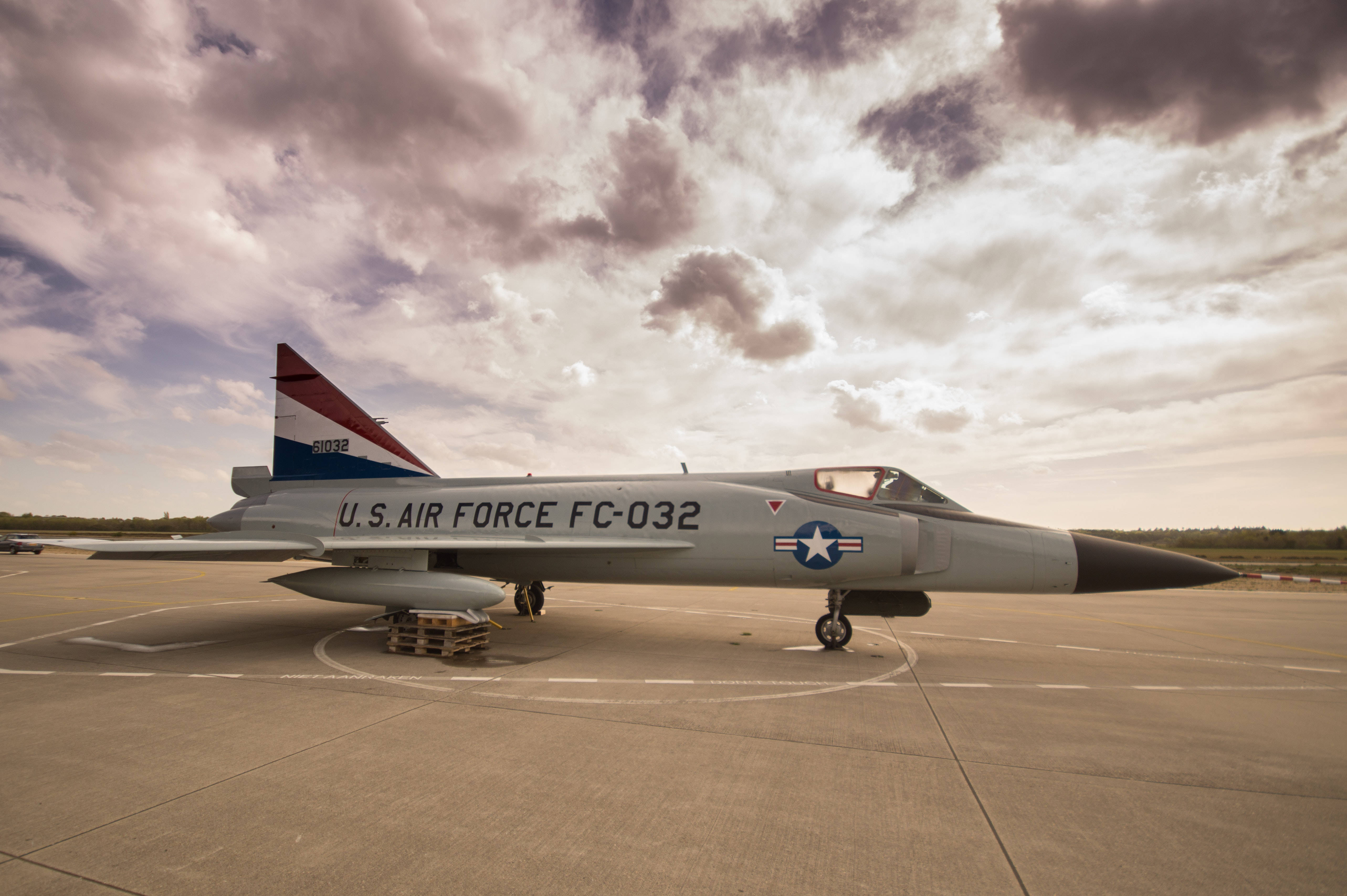 Air Force 桌布 壁紙 — 一架美國空軍戰鬥機在日落時分戲劇性的多雲天空下停在機場停機坪上。