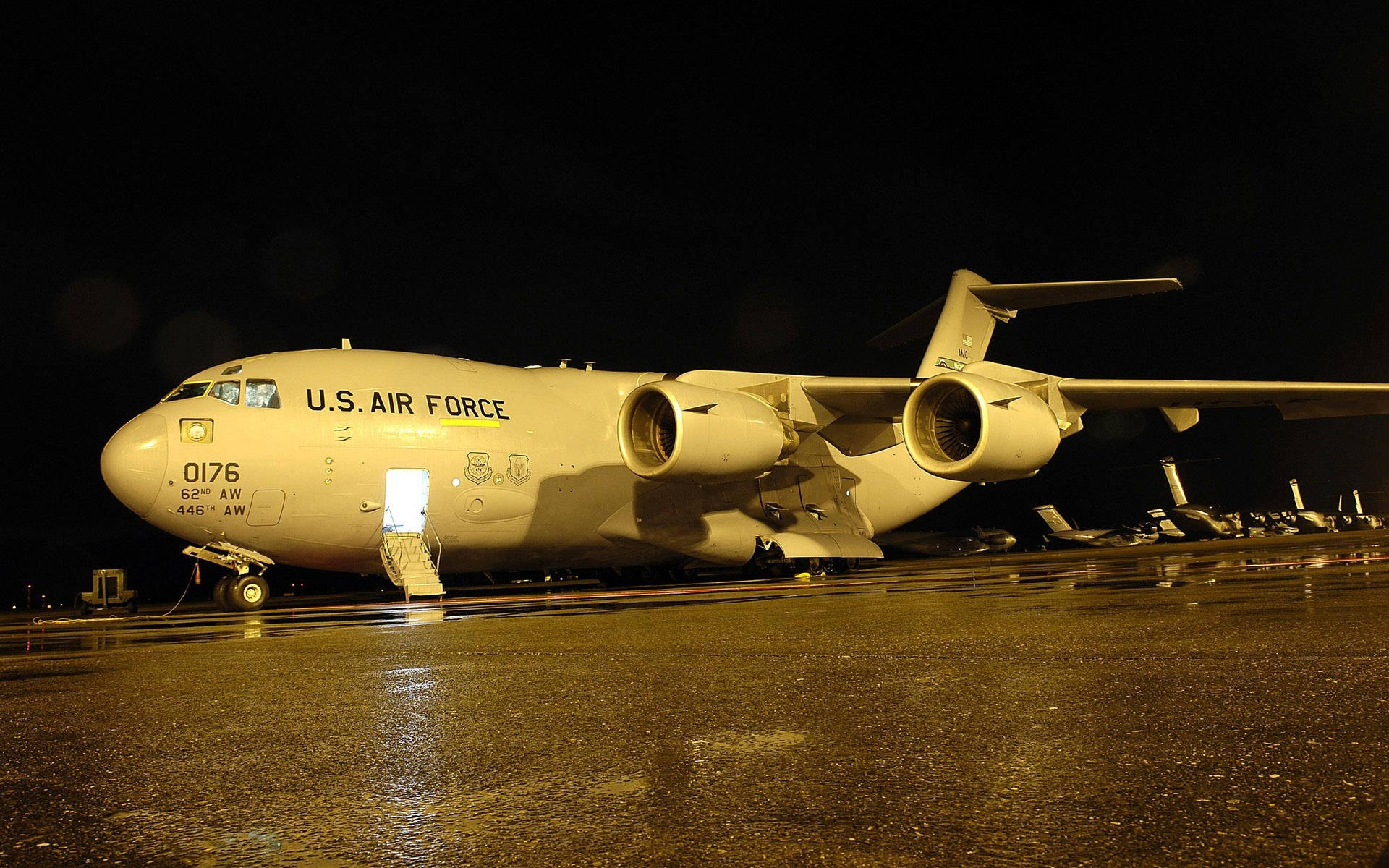 Air Force 桌布 壁紙 — 一架美國空軍貨機在漆黑的夜空下，被溫暖的燈光照亮在潮濕的停機坪上。