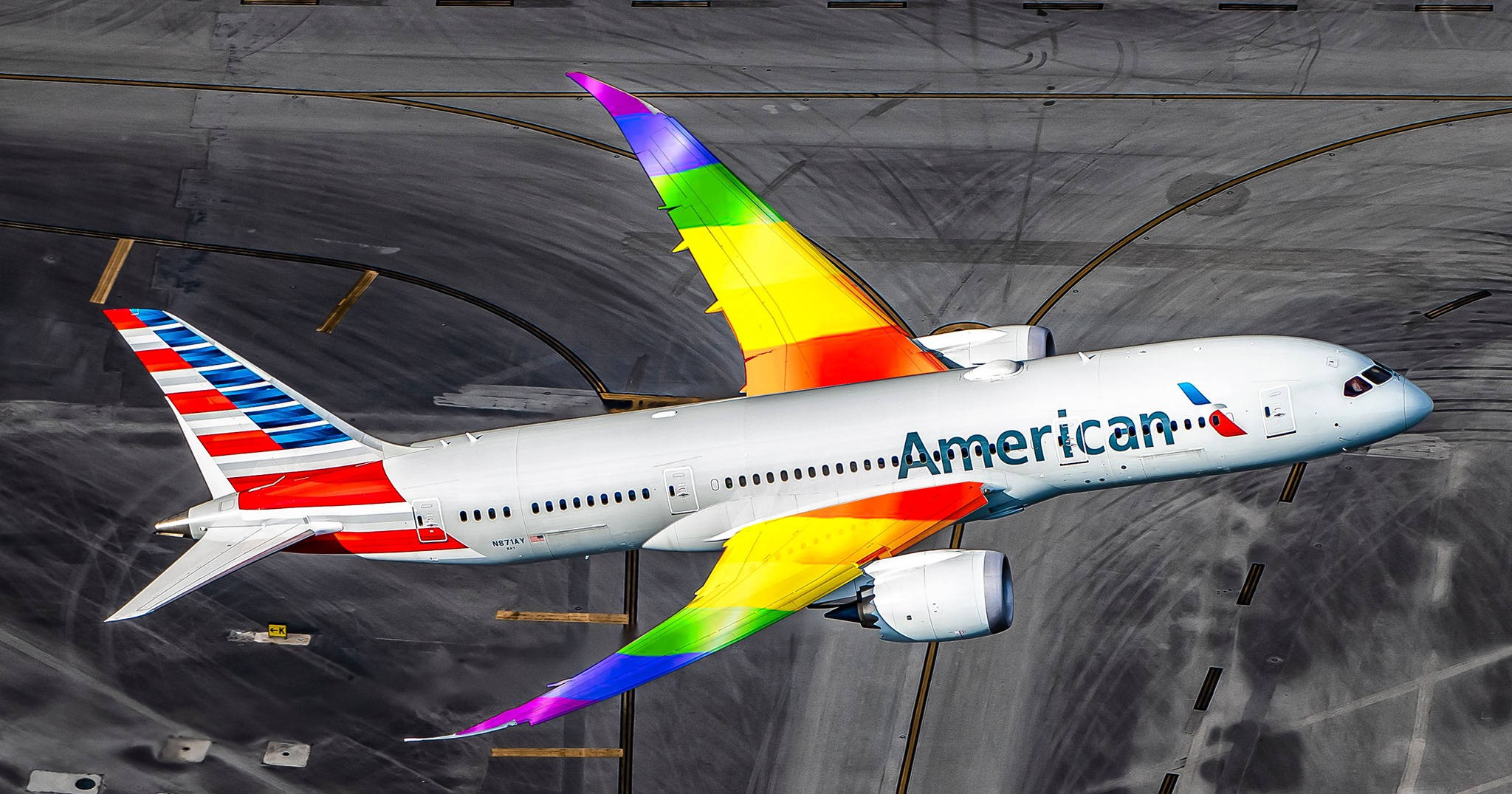 Airlines 桌布 壁紙 — 一架美國航空公司的飛機帶有彩虹色機翼，在明亮的日光下滑行在灰色的機場停機坪上。