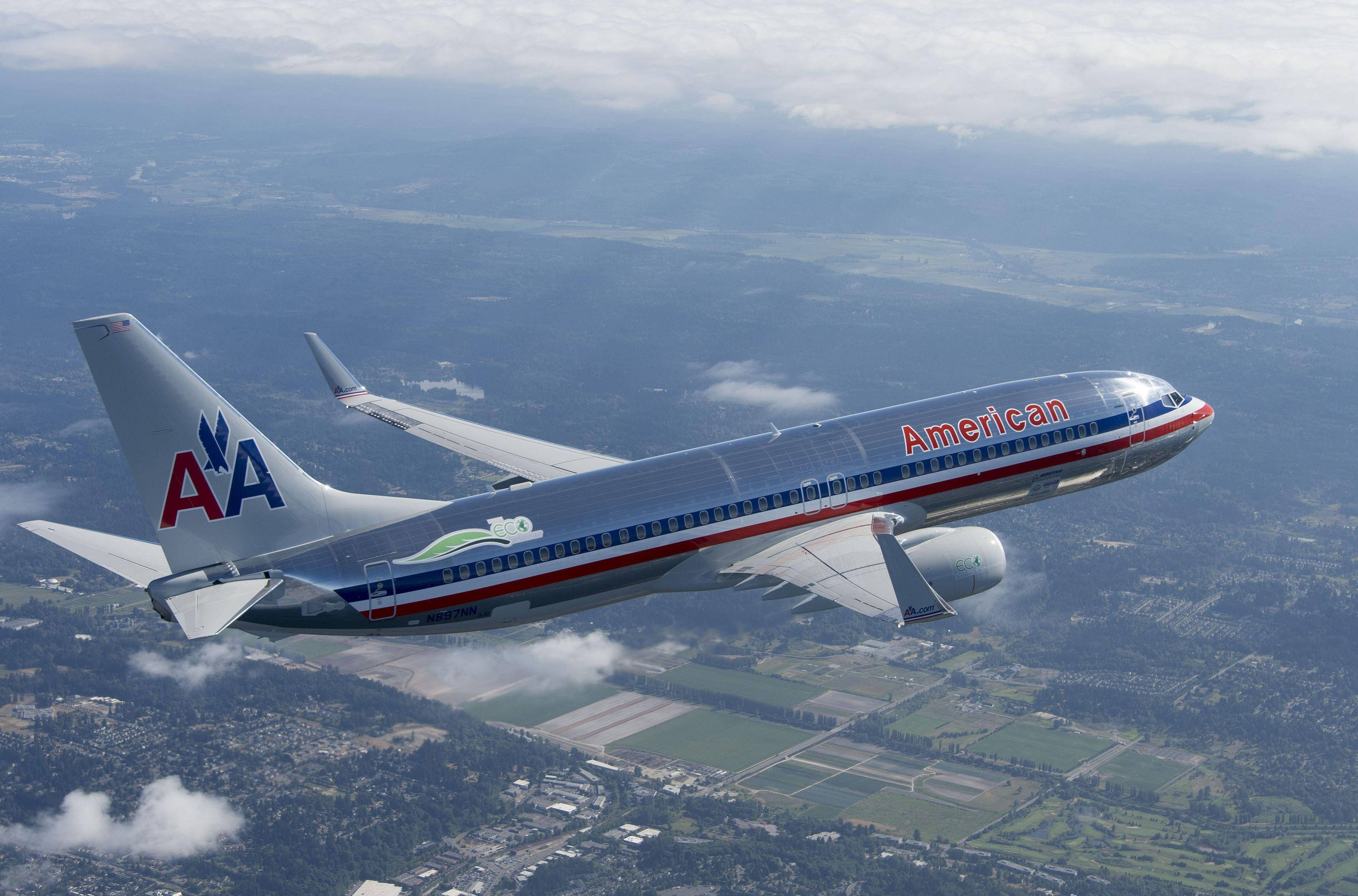 Airlines 桌布 壁紙 — 一架美國航空噴射機在陰天之下，翱翔於由綠色田野和城鎮拼湊而成的景觀之上。