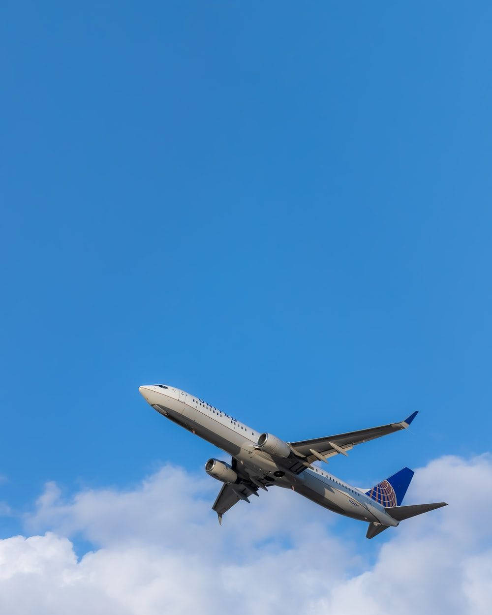 飛機 桌布 壁紙 — 一架聯合航空噴射機在下方蓬鬆白雲襯托下，強勁地攀升至鮮豔藍天。