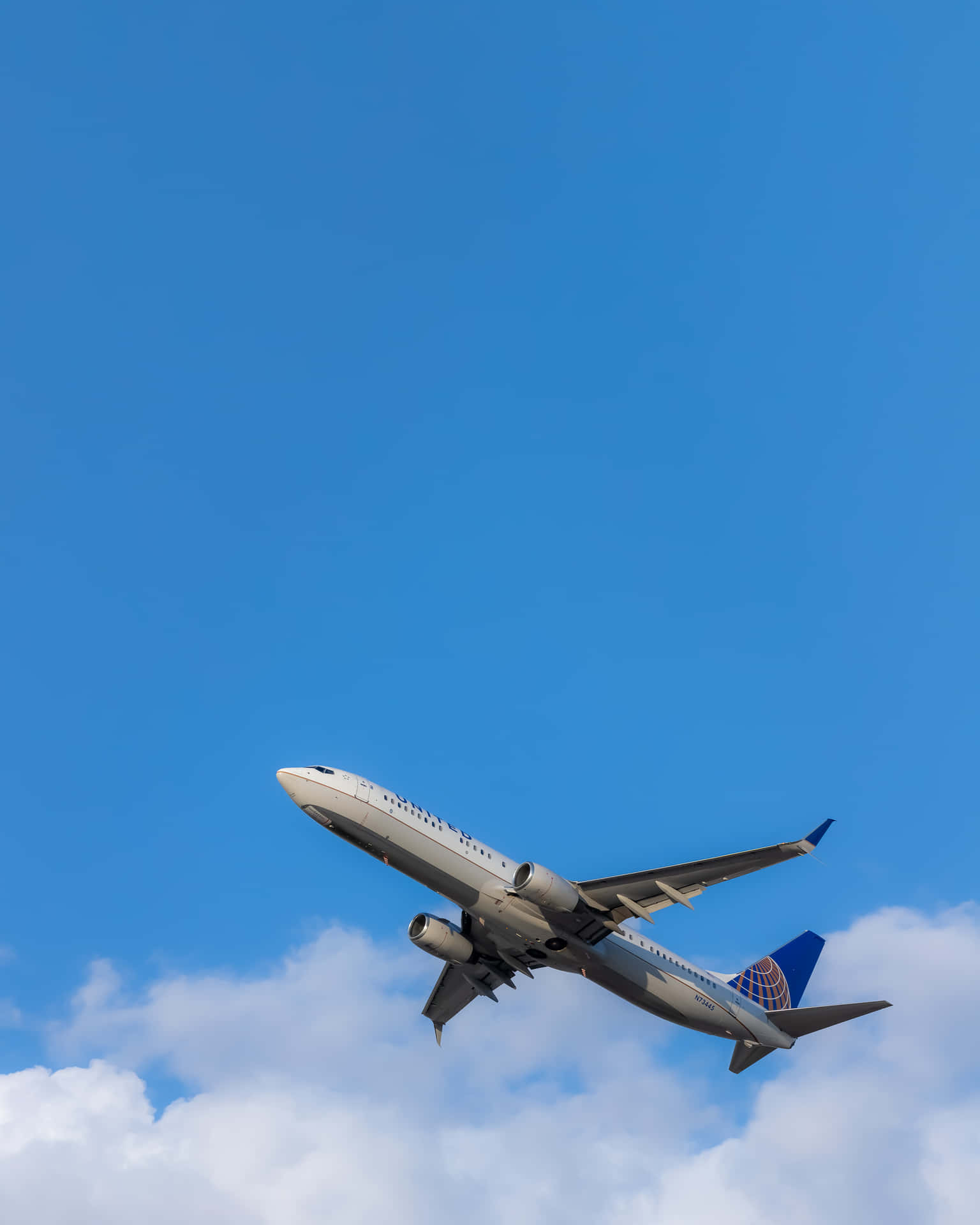 飛機 桌布 壁紙 — 一架聯合航空噴射機穿過清澈的藍天，下方有蓬鬆的白雲。