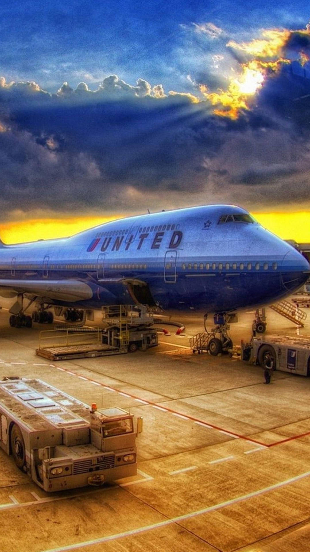  壁紙 — 一架聯合航空波音747停泊在停機坪上，背景是壯麗的日落天空，陽光穿透雲層形成耀眼的光芒。