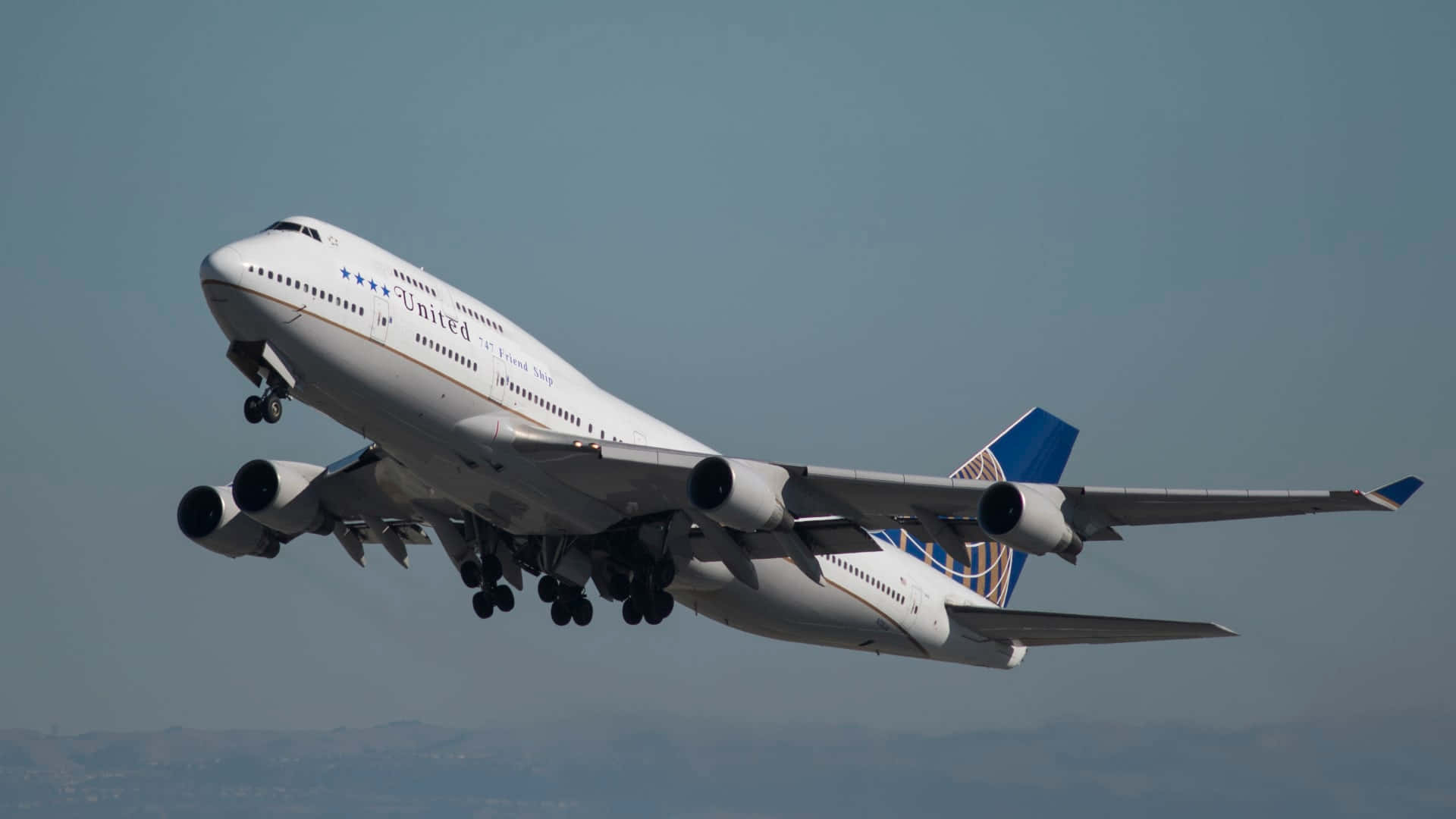 背景 桌布 壁紙 — 一架聯合航空波音747正在起飛，起落架伸出，背景是遠山和朦朧的天空。