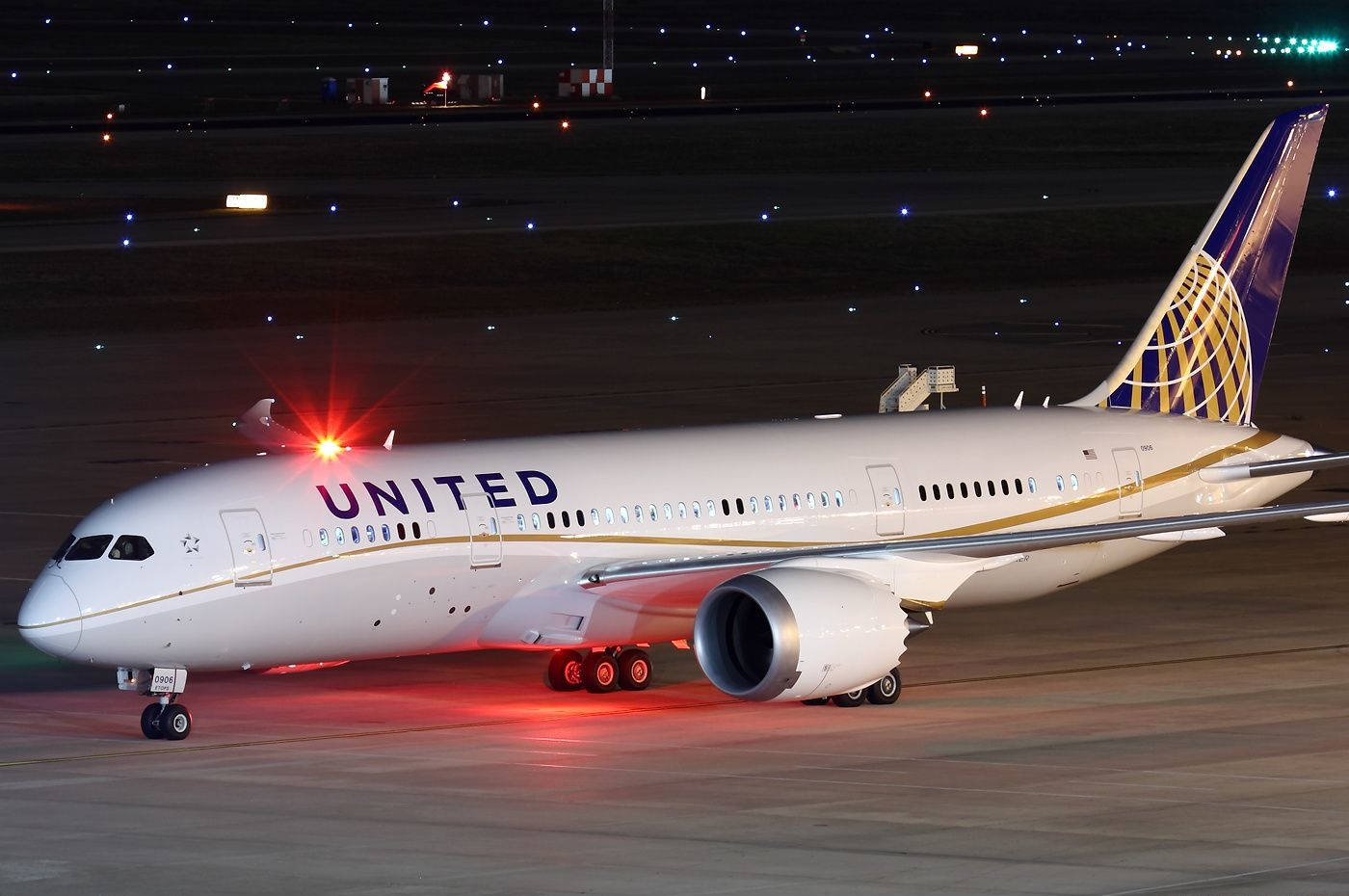 Airport 桌布 壁紙 — 一架聯合航空波音787夢幻客機在夜間黑暗的機場停機坪上，在紅色著陸燈下閃耀。