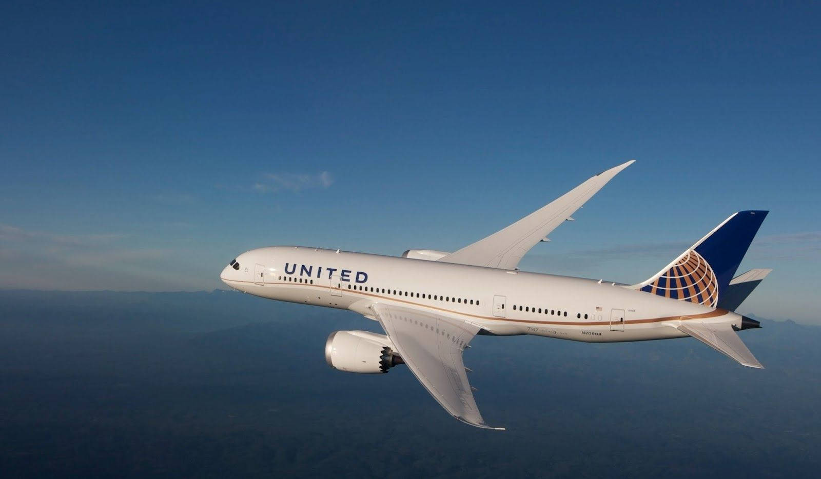 Plane 桌布 壁紙 — 一架聯合航空波音787夢想客機在朦朧海岸線上空，優雅地翱翔於清澈藍天。