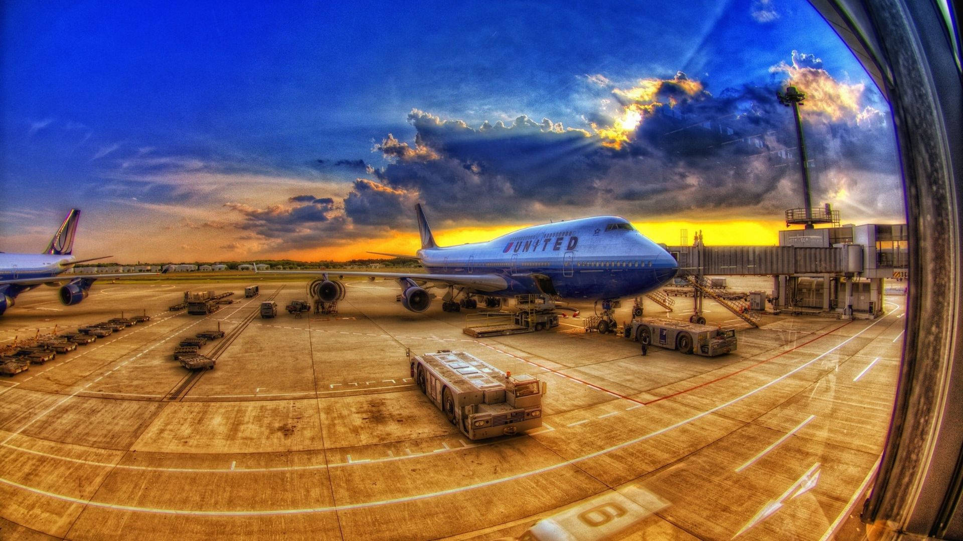 Runway 桌布 壁紙 — 一架聯合航空珍寶客機在充滿活力的日落時分停靠在機場閘口，伴隨著戲劇性的雲層和魚眼鏡頭變形。