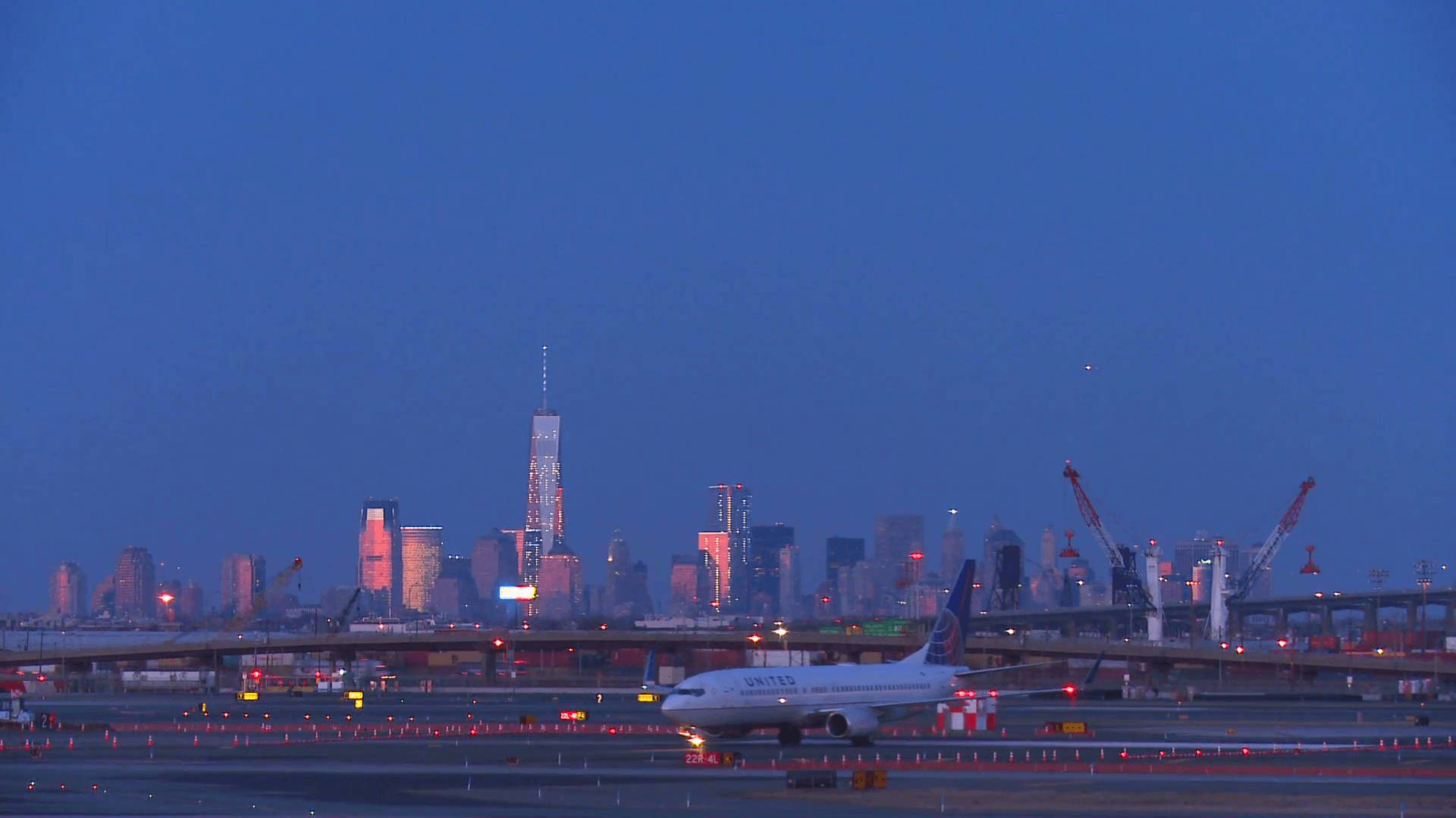 Airport 桌布 壁紙 — 一架聯合航空飛機在黃昏時分在機場停機坪滑行，背景是燈火通明的紐約市天際線。