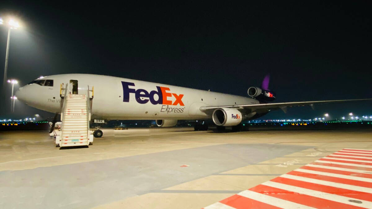 聯邦快遞 桌布 壁紙 — 一架聯邦快遞貨機在夜間停在機場停機坪上，附有登機梯，背景中跑道燈閃爍。