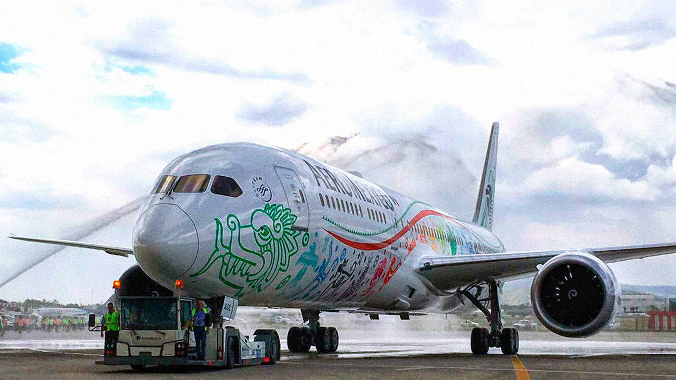Plane 桌布 壁紙 — 一架色彩繽紛的墨西哥航空公司飛機在多雲的天空下，在濕滑的停機坪上接受水砲禮炮慶祝。