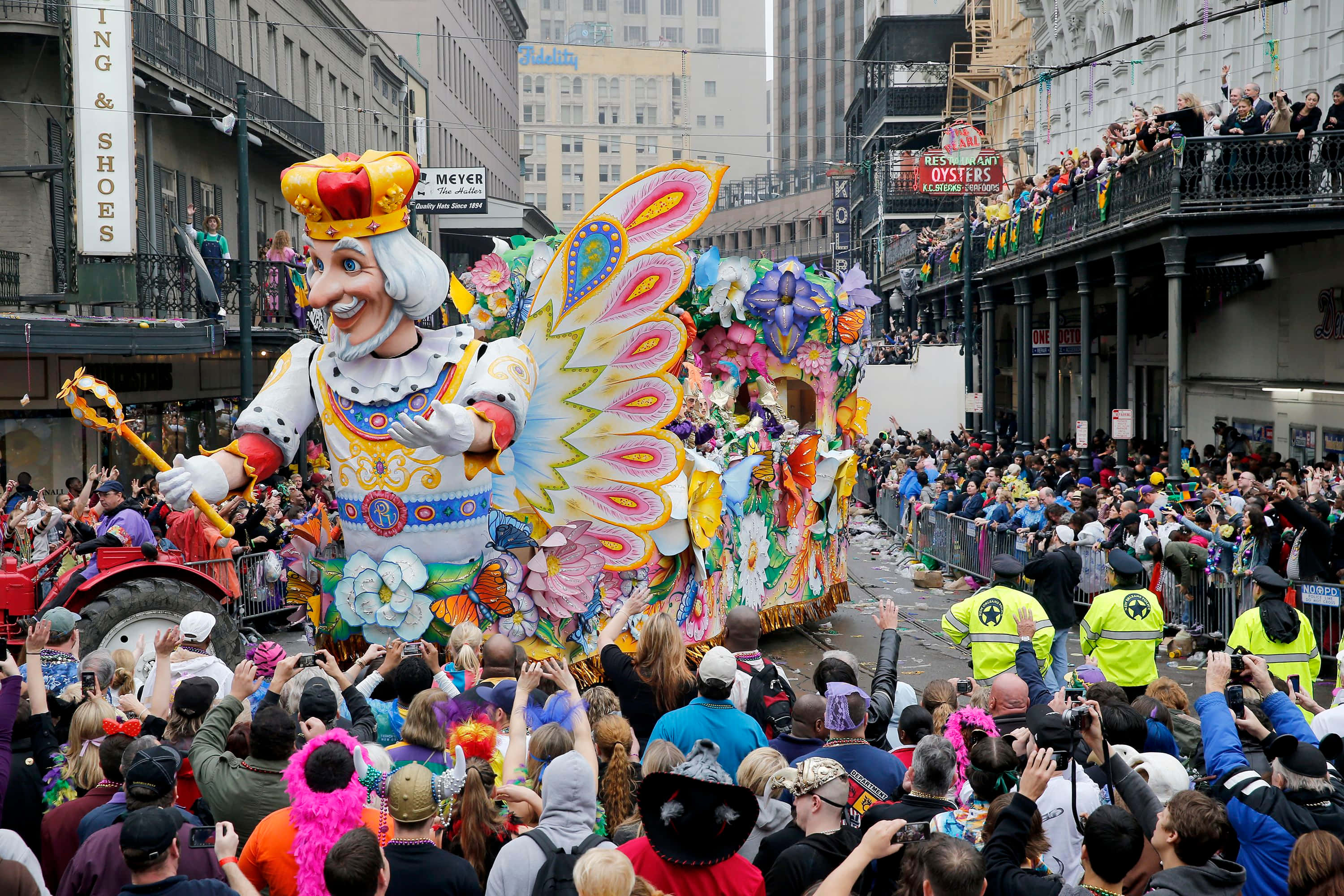 Mardi Gras 桌布 壁紙 — 一架色彩繽紛的狂歡節花車，上面有一個巨大微笑的國王，長著彩色翅膀，穿過紐奧良擁擠的街道。