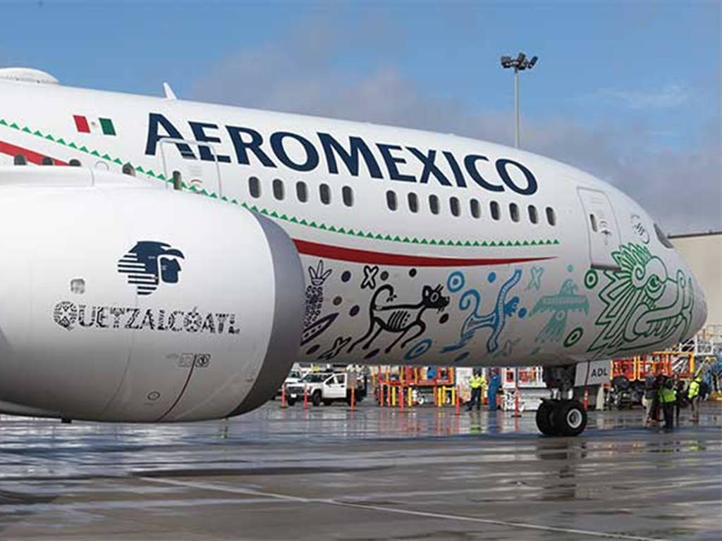 Airport 桌布 壁紙 — 一架色彩鮮豔的 Aeromexico 飛機，帶有 Guetzalcoatl 藝術作品，停放在潮濕的停機坪上，天空部分多雲。