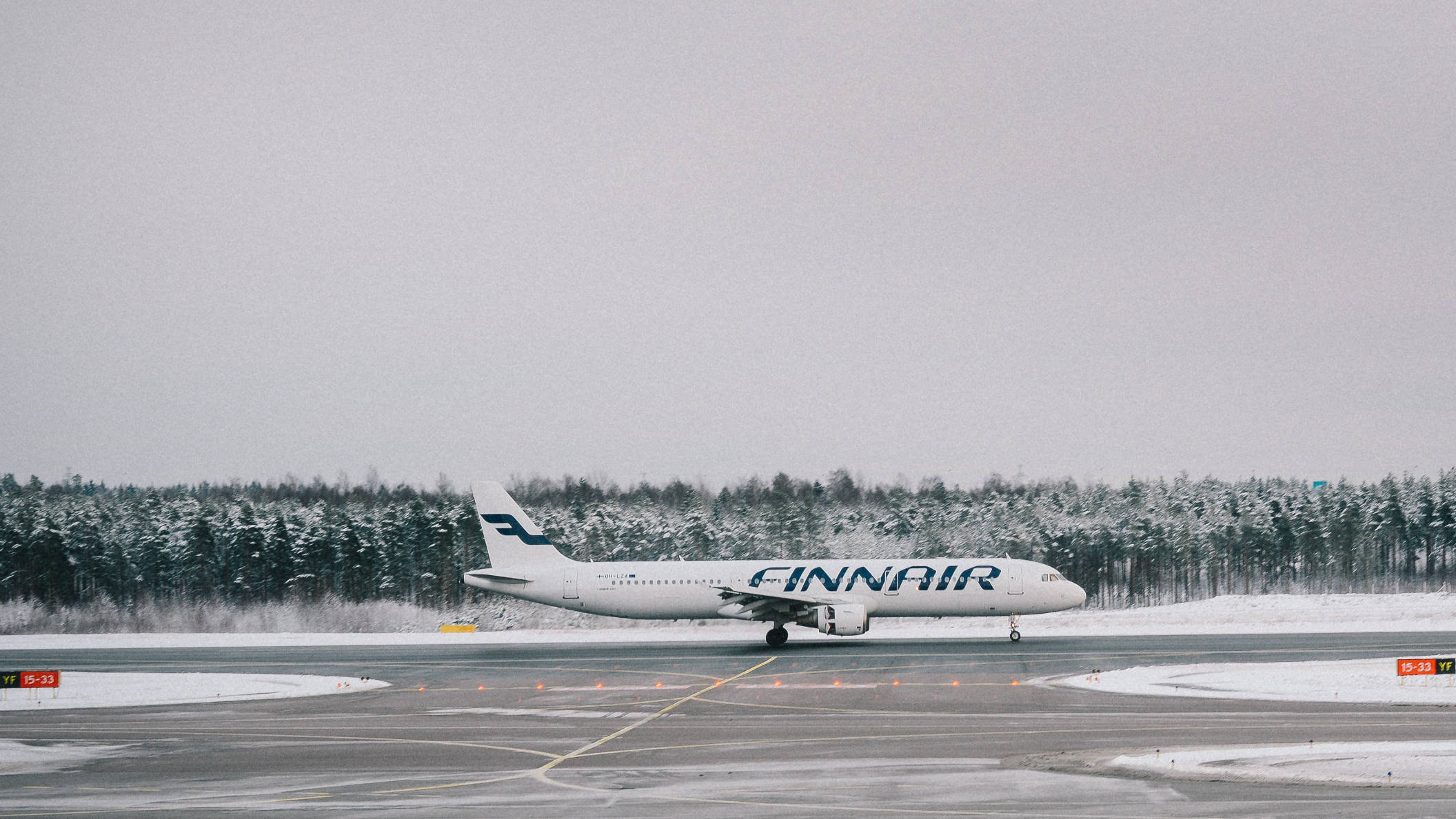 Runway 桌布 壁紙 — 一架芬蘭航空的飛機停在灑滿雪的跑道上，背景是白雪覆蓋的樹林和陰天。