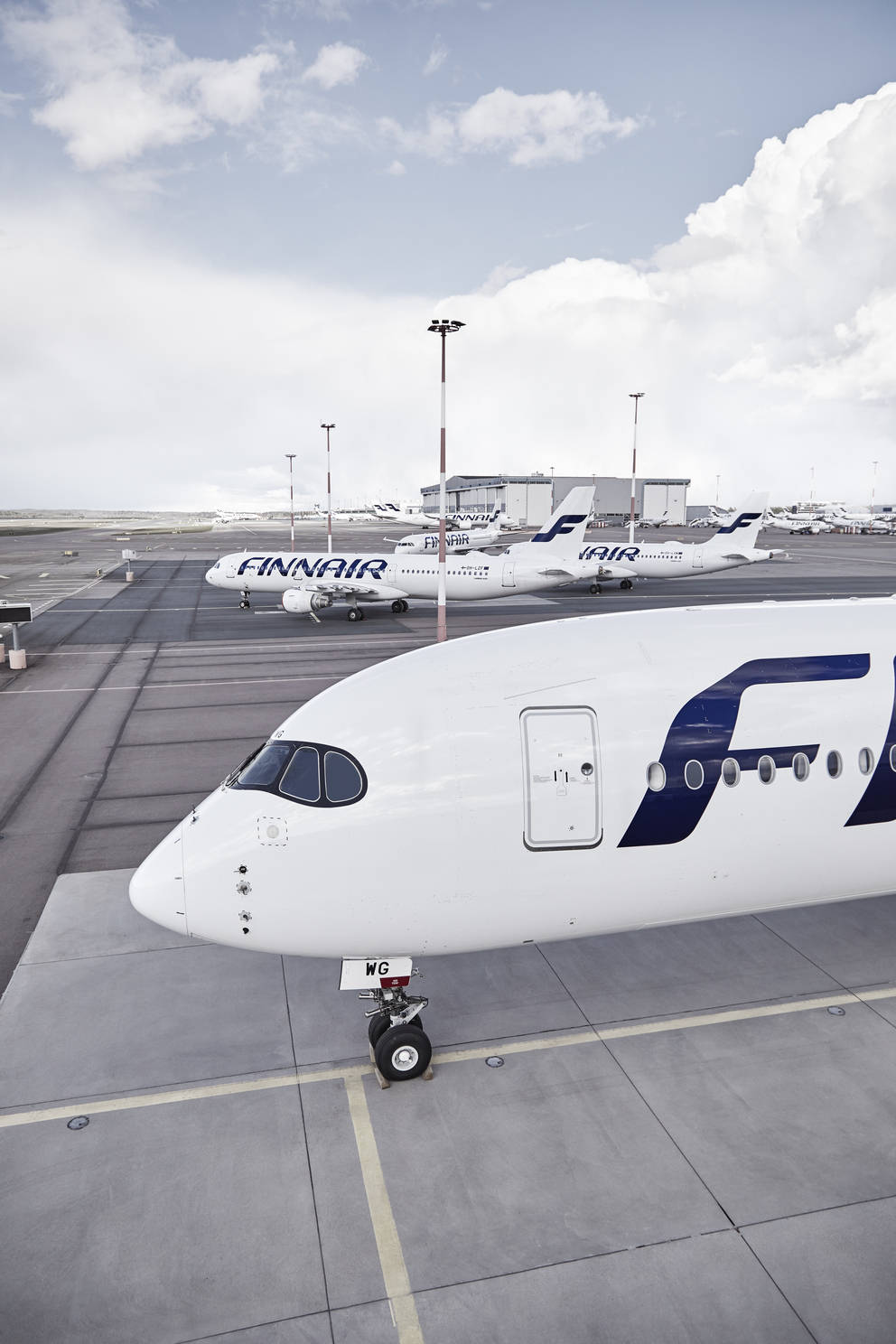 飛機 桌布 壁紙 — 一架芬蘭航空的飛機顯眼地停在機場停機坪上，其他飛機和機庫在部分多雲的天空下清晰可見。