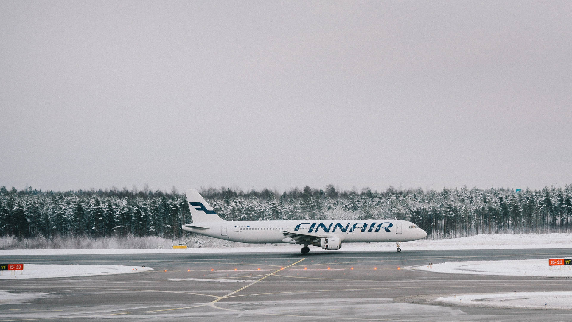 飛機 桌布 壁紙 — 一架芬蘭航空飛機停在灑滿雪的跑道上，背景是陰天下一片白雪覆蓋的樹林。