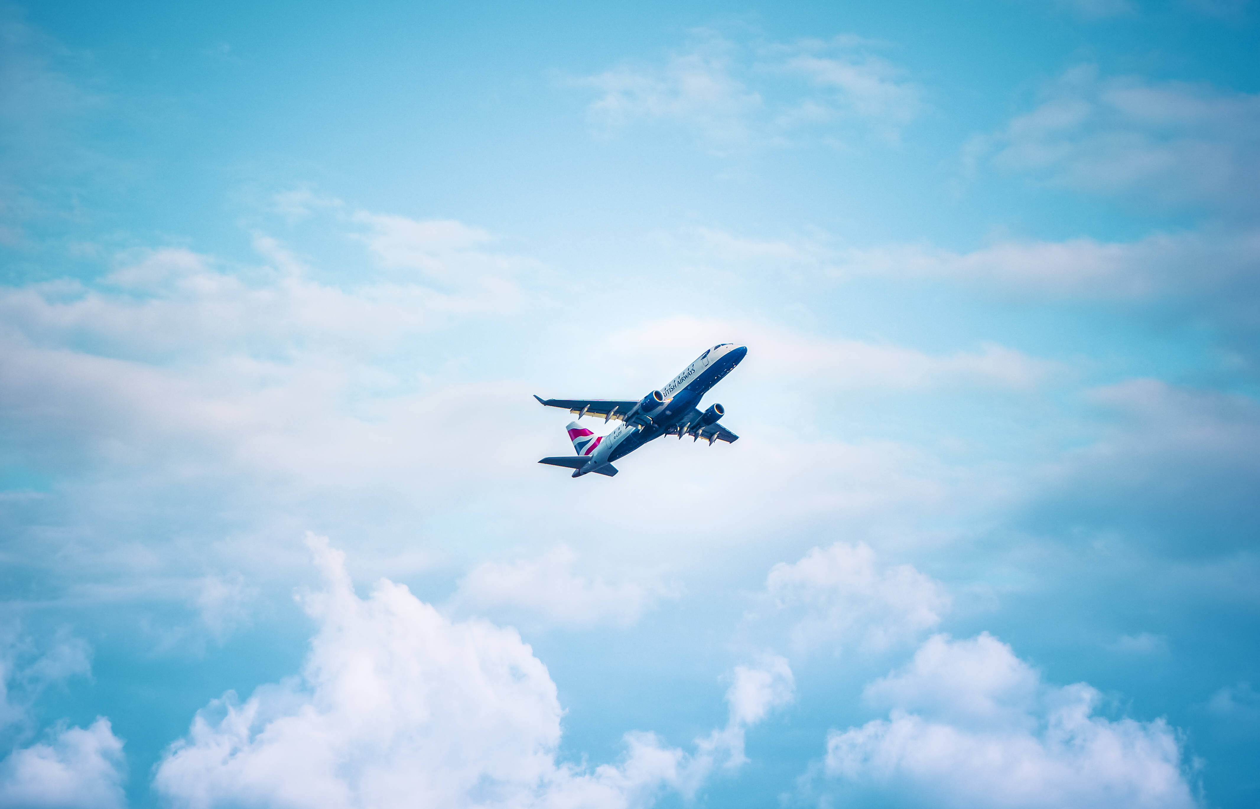 飛機 桌布 壁紙 — 一架英國航空公司的飛機在鮮豔的藍天背景下，優雅地在蓬鬆的白雲上方翱翔。