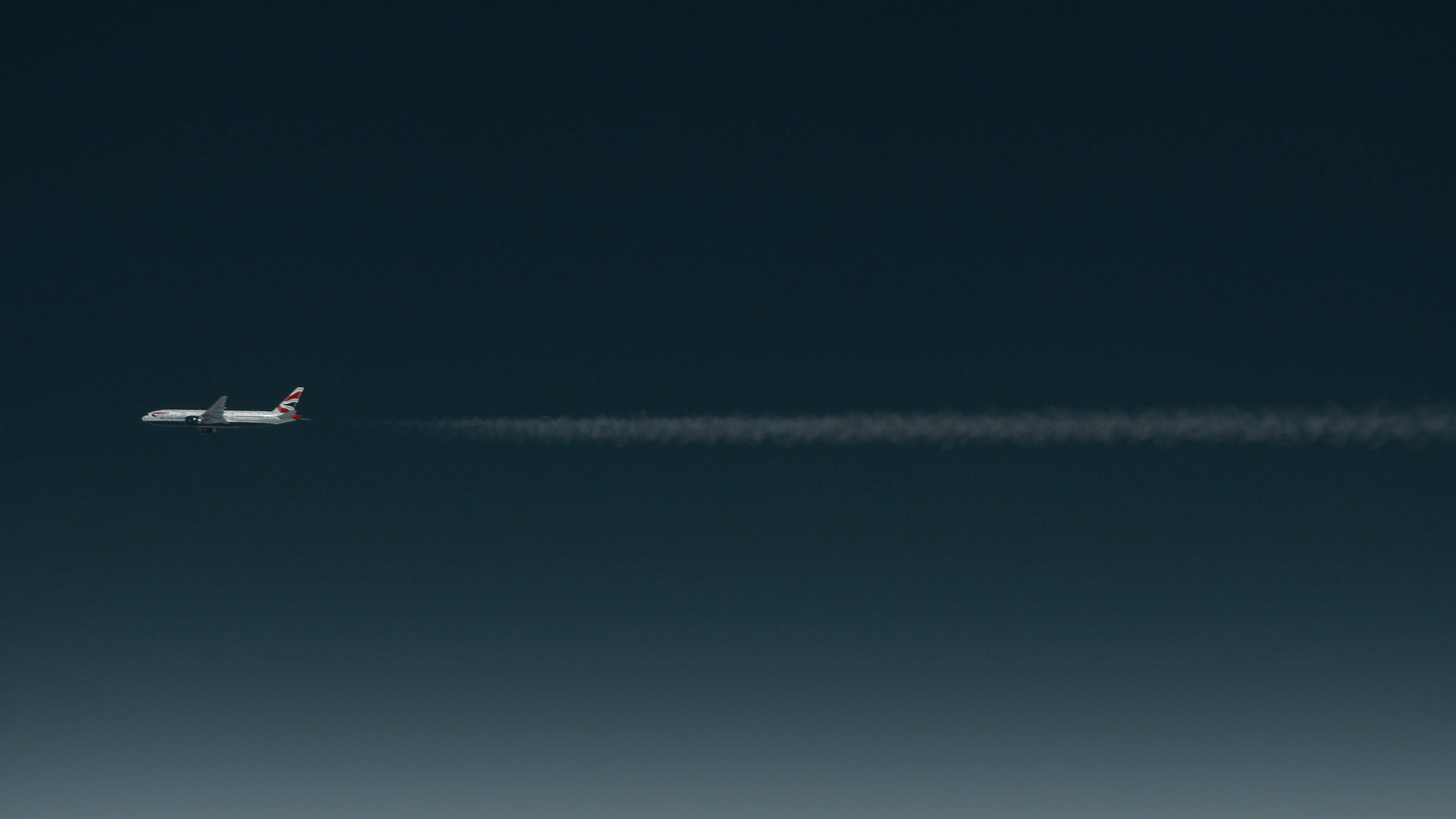 Plane 桌布 壁紙 — 一架英國航空公司的飛機獨自飛翔在深藍色漸變的天空中，留下一條長長的白色的凝結尾跡。