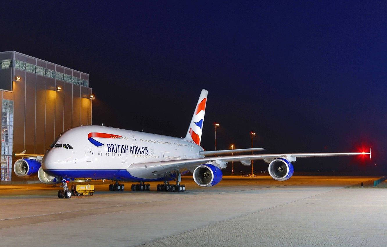 飛機 桌布 壁紙 — 一架英國航空的空中巴士A380在夜間於機場停機坪上，旁邊是一座現代化的航廈，被燈光照亮。