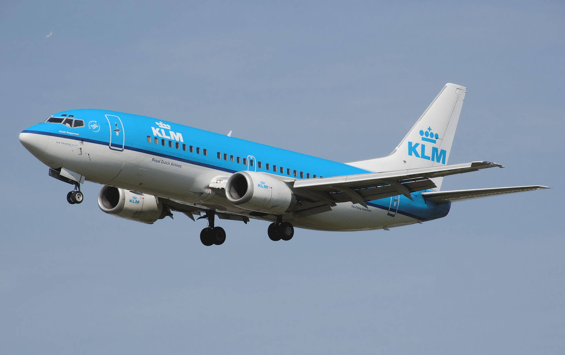  壁紙 — 一架荷蘭皇家航空的波音737以藍白塗裝，在起落架放下時，向著清澈的淡藍色天空上升。