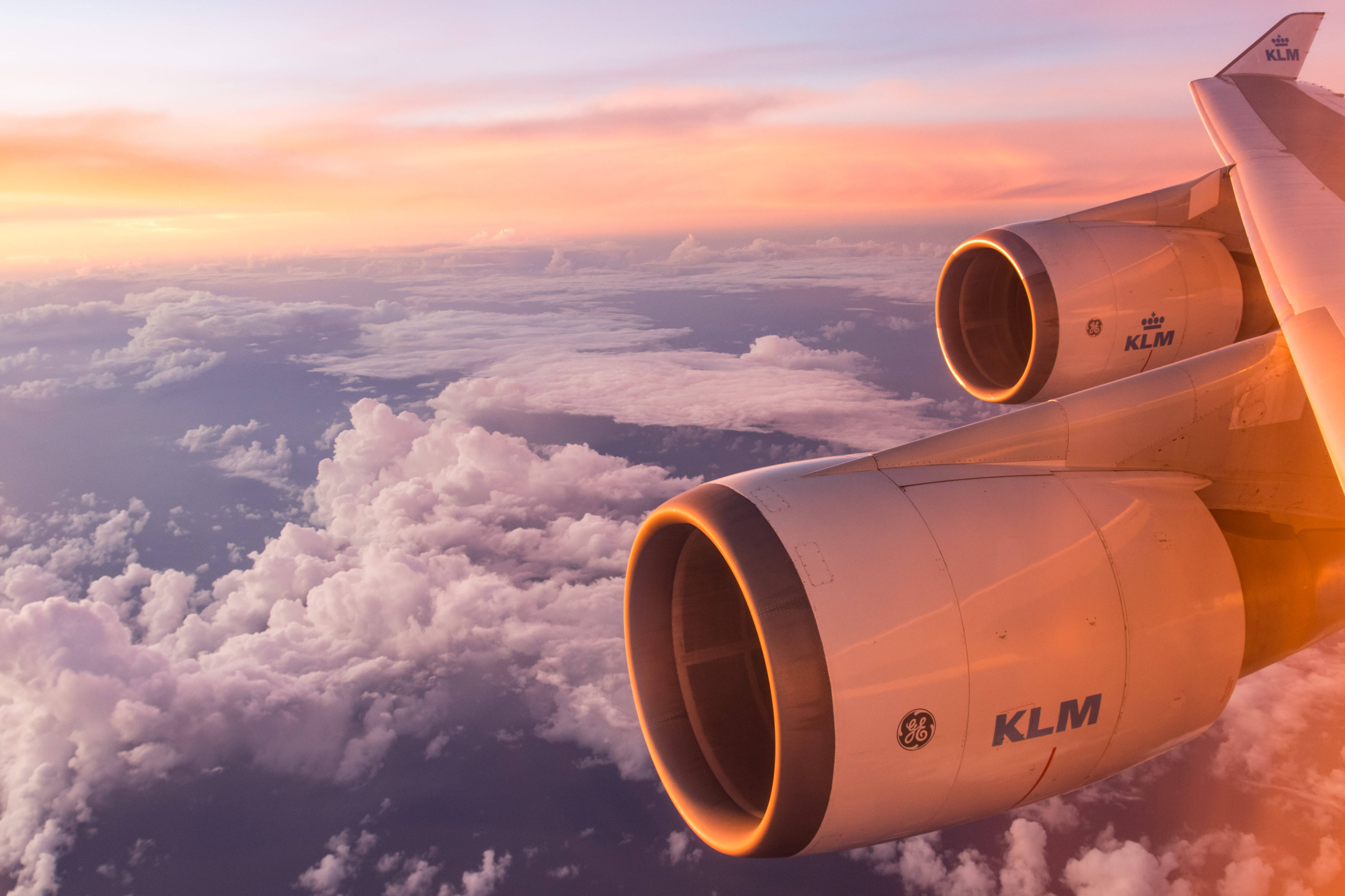 Plane 桌布 壁紙 — 一架荷蘭皇家航空的飛機引擎在夕陽天空下溫暖地發光，飛越蓬鬆的白雲。