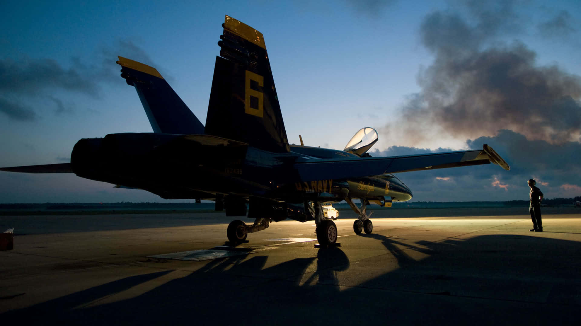 US Navy 桌布 壁紙 — 一架藍天使噴射機在暮色天空的襯托下呈現剪影，附近停機坪上有一個孤獨的身影站立。