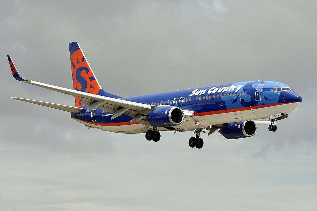 飛機 桌布 壁紙 — 一架藍橙色塗裝的太陽鄉村航空波音737正在多雲的天空中放下起落架下降。