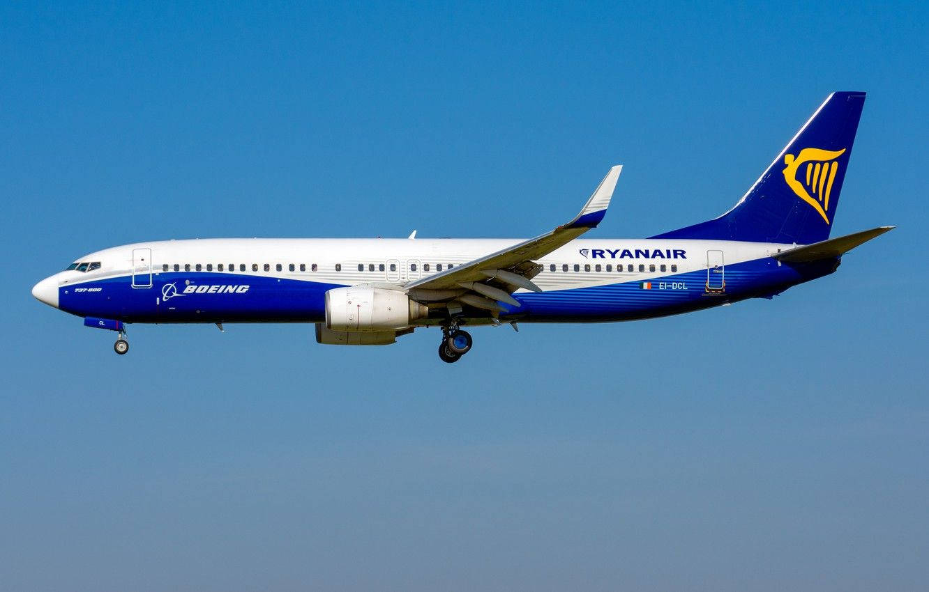 飛機 桌布 壁紙 — 一架藍白塗裝的瑞安航空波音 737 在日間飛行中優雅地傾斜，背景是清澈的蔚藍天空。