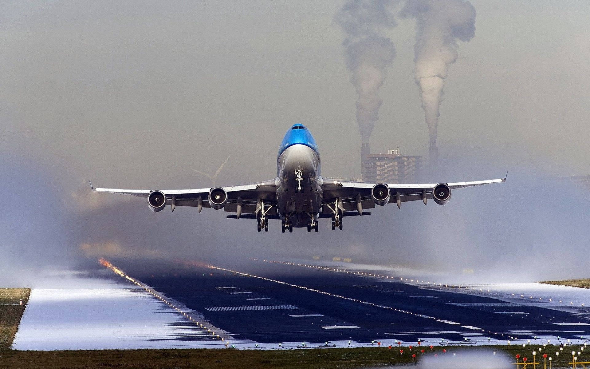 Airport 桌布 壁紙 — 一架藍白相間的珍寶客機從積雪跑道起飛，遠處工業煙囪冒著煙。