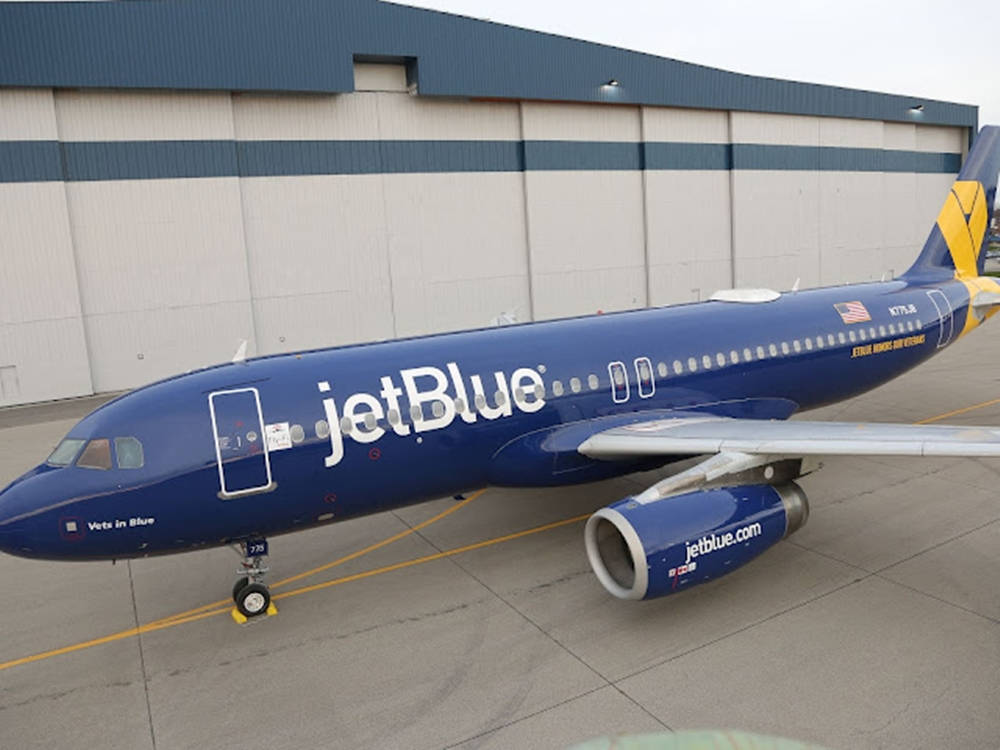 Plane 桌布 壁紙 — 一架藍色jetBlue飛機停放在停機坪上，前方是一個大型機庫，天空多雲。