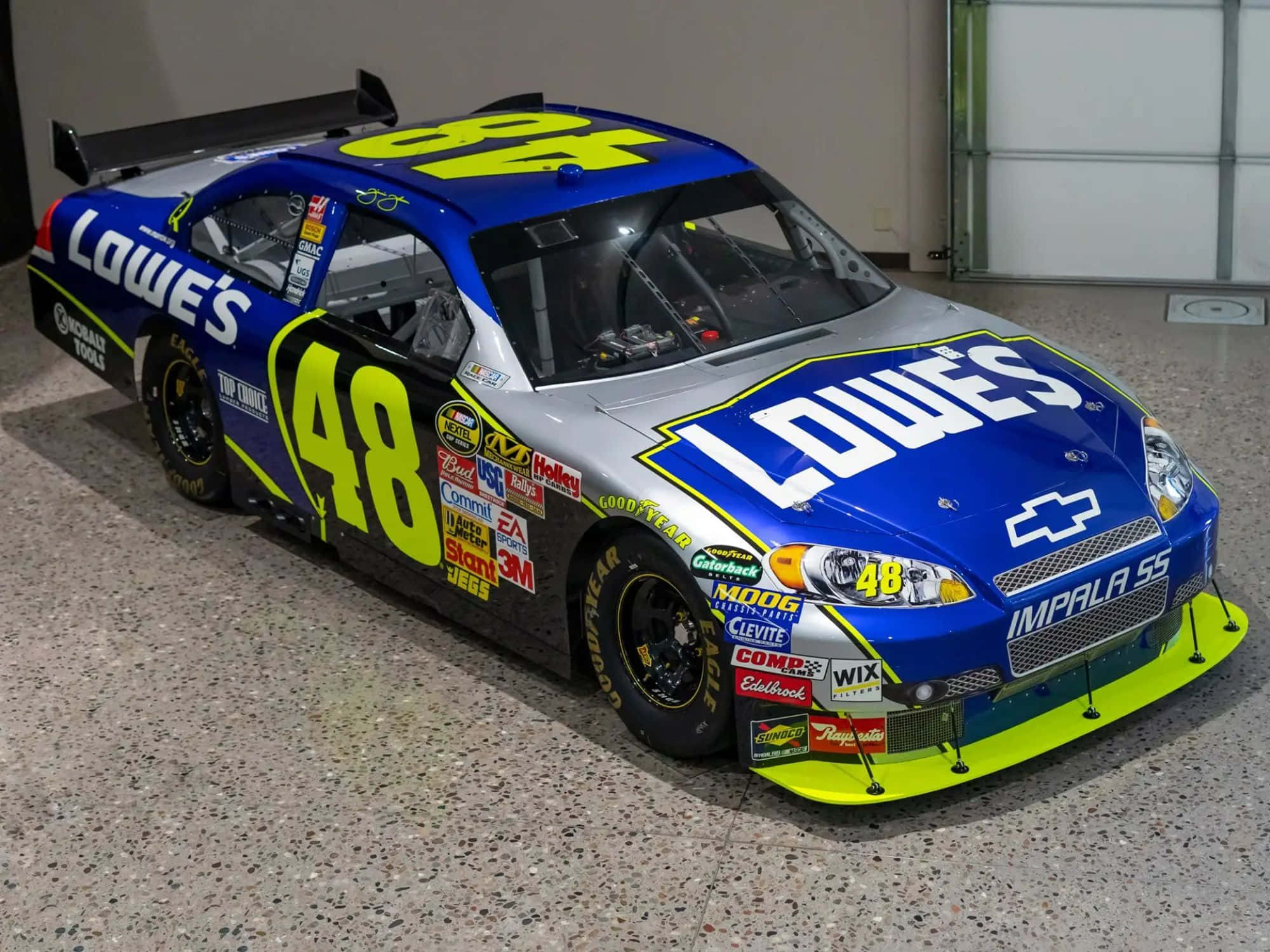 nascar 桌布 壁紙 — 一架藍色和銀色的NASCAR賽車，帶有48號和Lowe's品牌，在室內有斑點的地板上展示。