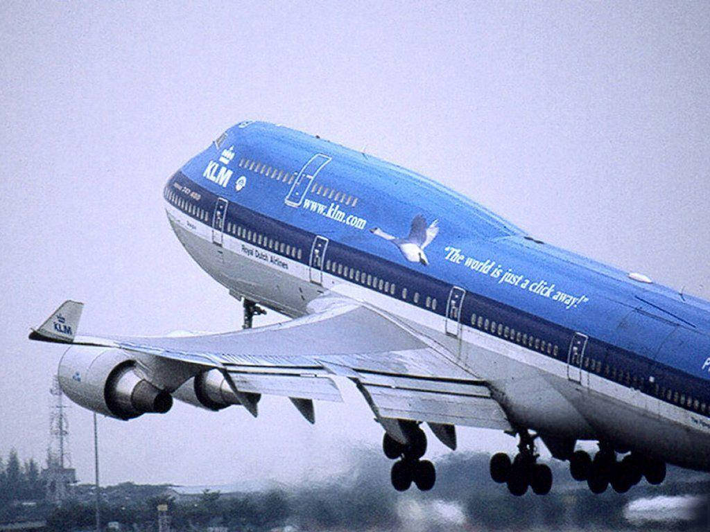 Airport 桌布 壁紙 — 一架藍色塗裝的KLM波音747飛機放下起落架，低飛過朦朧的城市景觀。