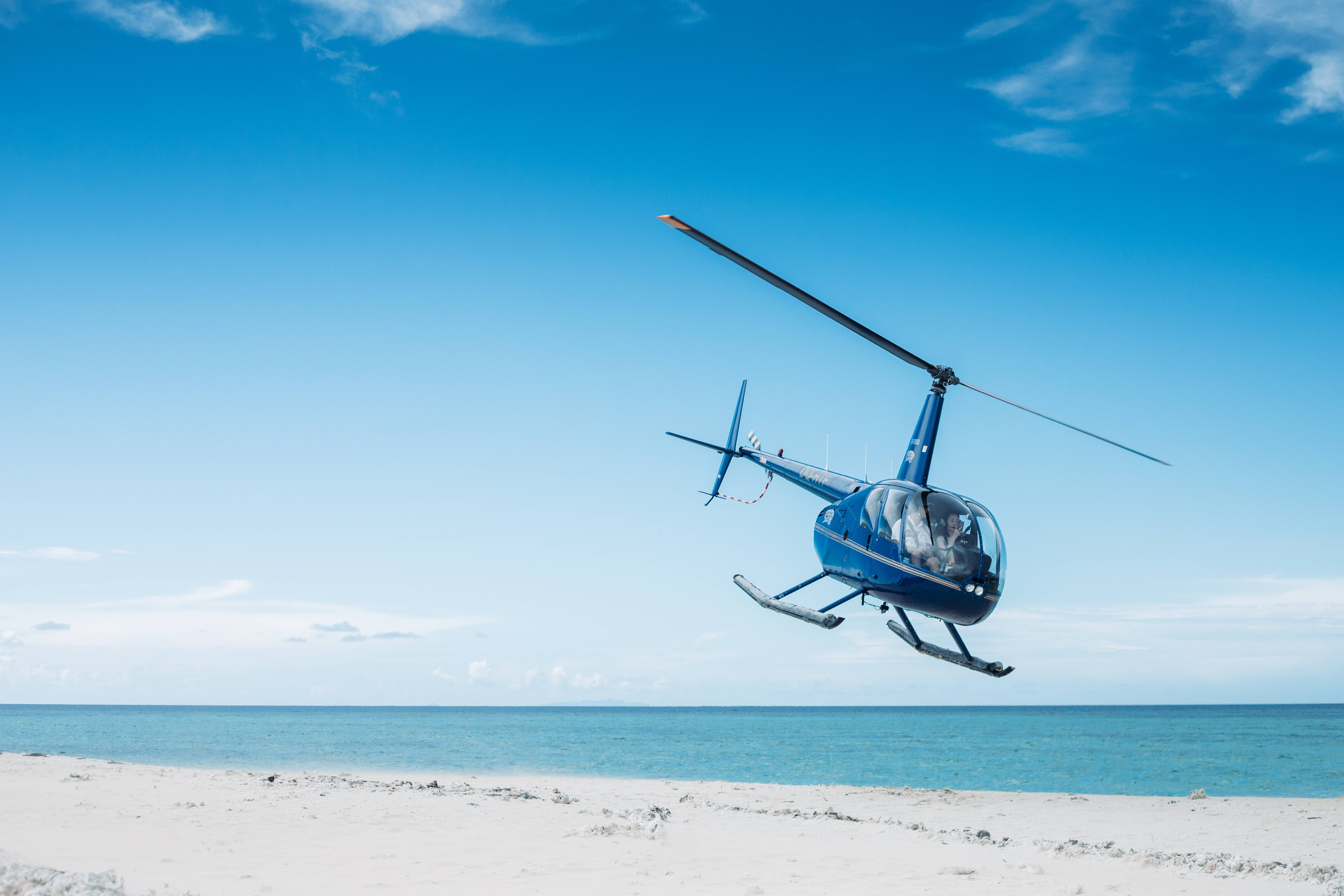 Helicopter 桌布 壁紙 — 一架藍色直升機低空盤旋在純淨的白色沙灘上，伴隨著碧綠的海洋和清澈的藍天。