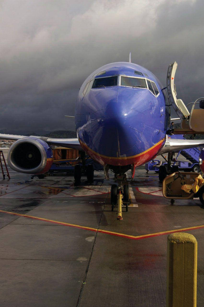 Southwest 桌布 壁紙 — 一架藍色西南航空噴射機停在潮濕的停機坪上，天空風暴密佈，登機梯已連接。