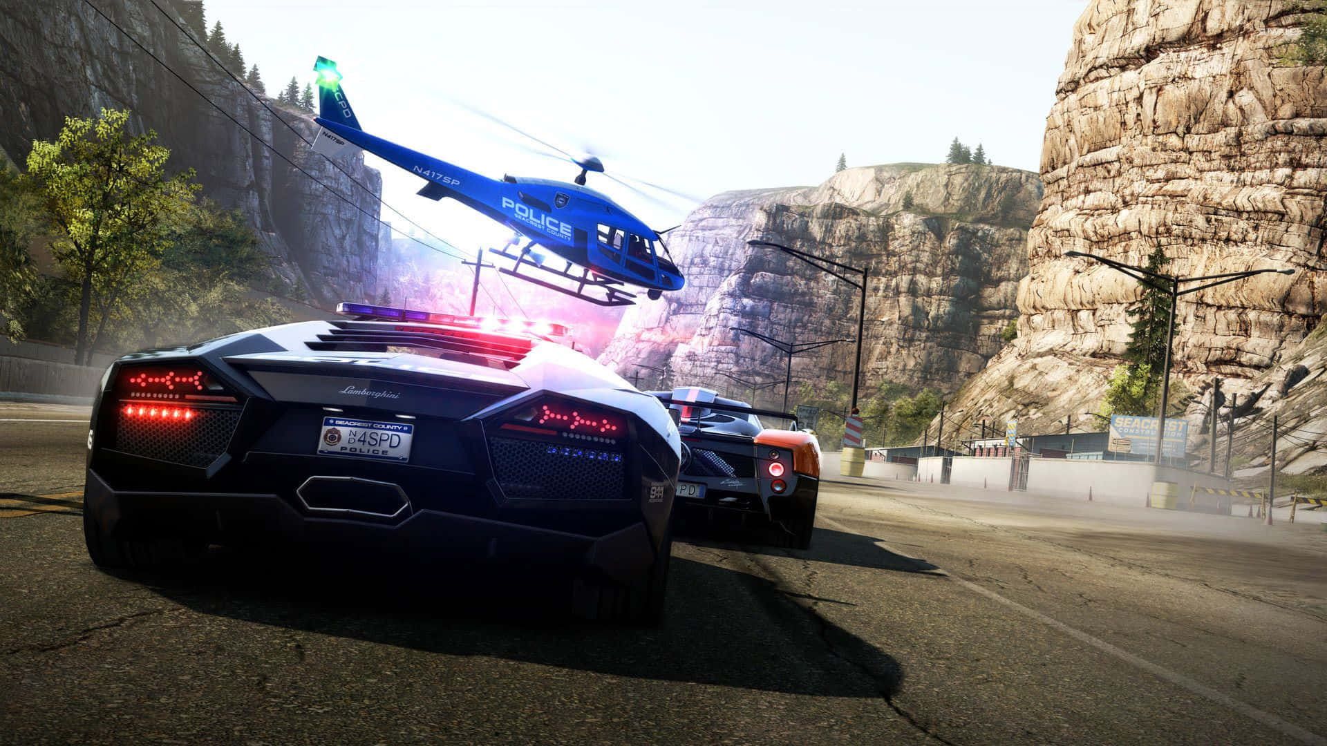 Best Need For Speed 桌布 壁紙 — 一架藍色警用直升機盤旋在一輛黑色藍寶堅尼Aventador上空，該車正被另一輛警車在山路上追捕。