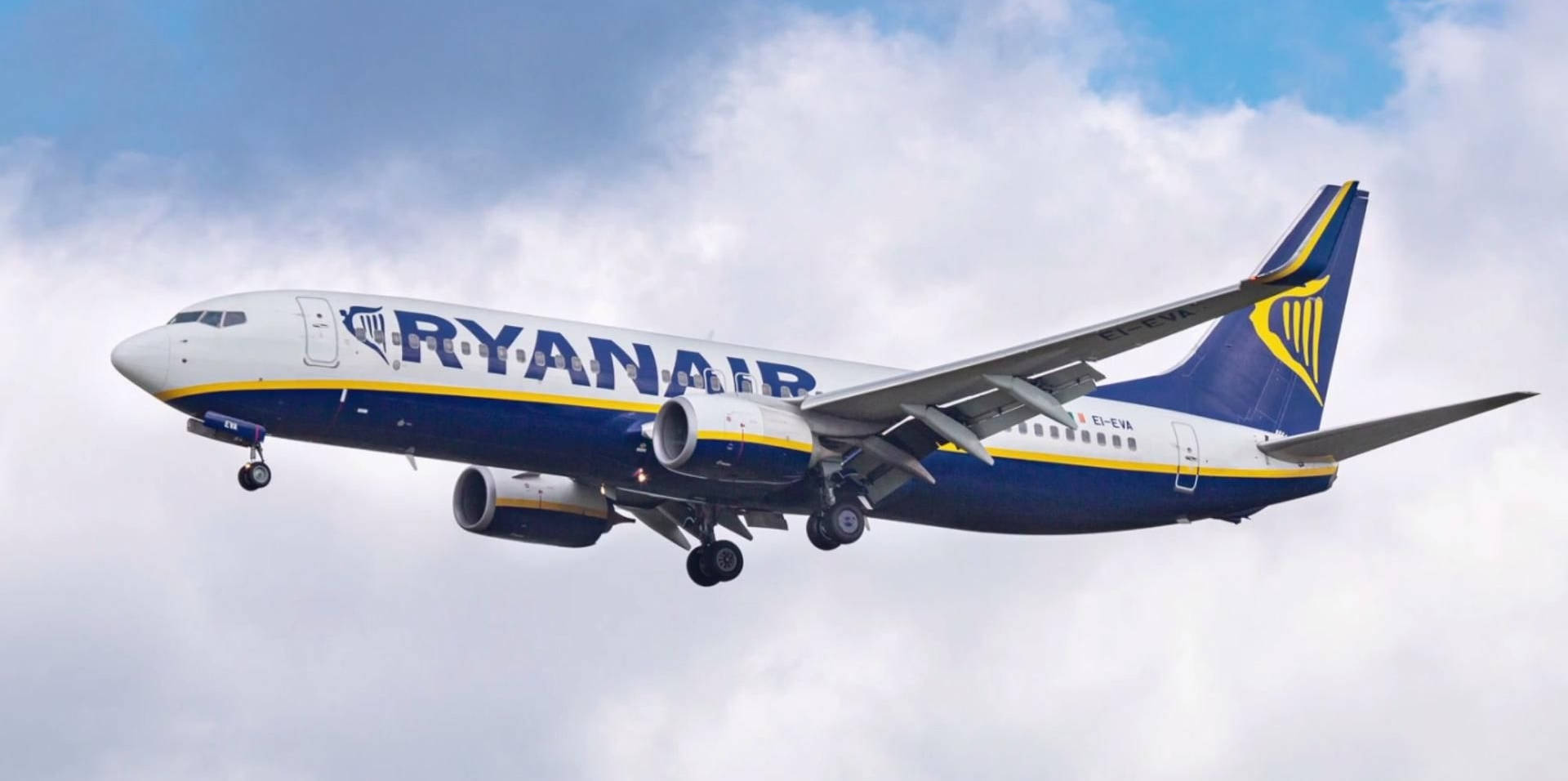 flying 桌布 壁紙 — 一架藍黃塗裝的瑞安航空客機在部分多雲的天空下低飛，起落架已放下。