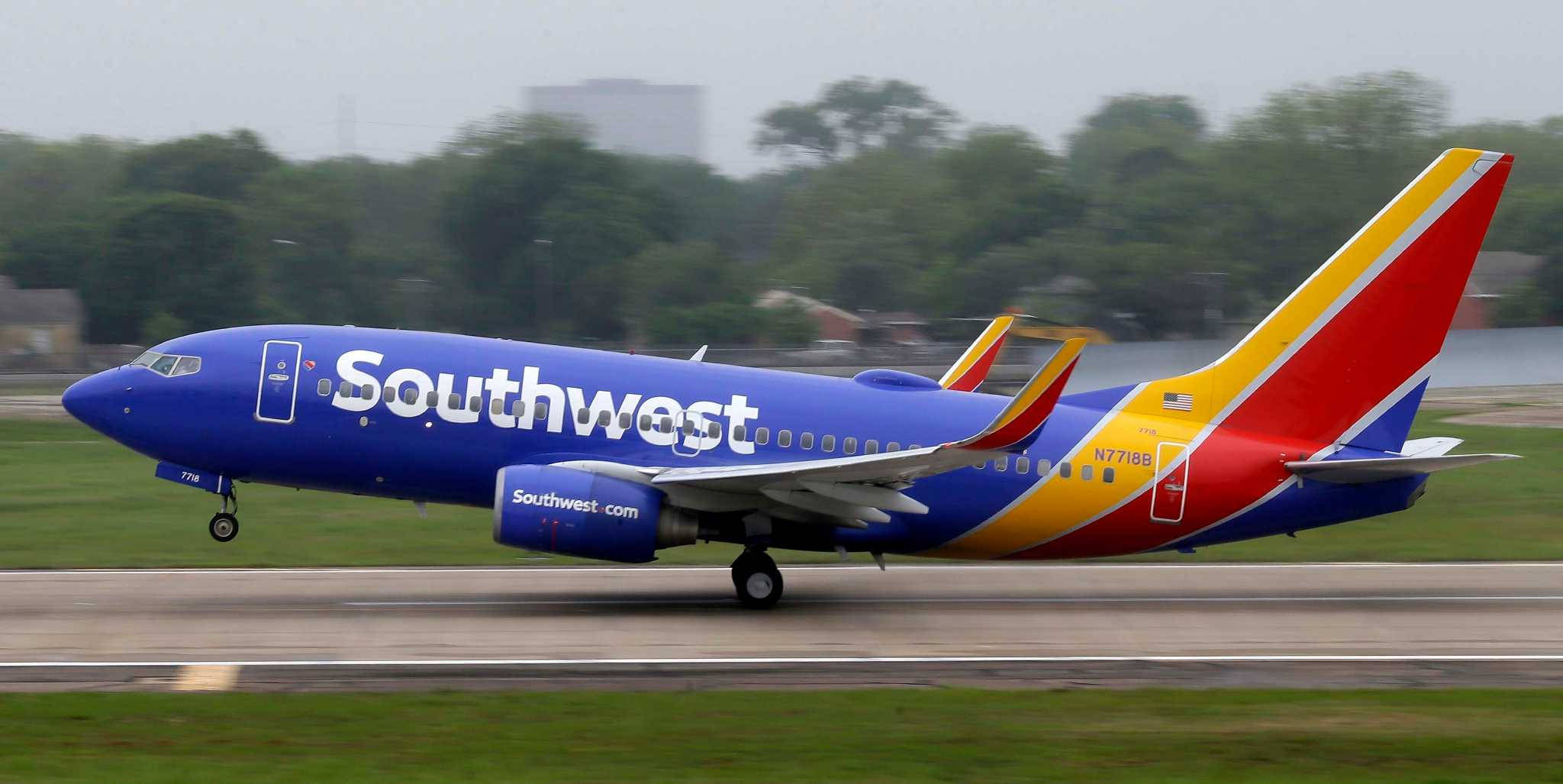 飛機 桌布 壁紙 — 一架西南航空波音737，採用藍、紅、黃色塗裝，在潮濕的跑道上滑行，背景有模糊的綠色樹木。