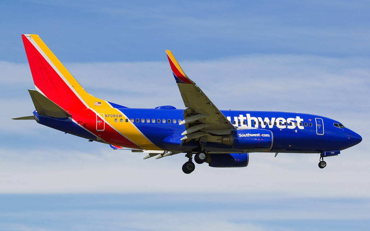 Southwest 桌布 壁紙 — 一架西南航空波音737以鮮豔的藍、紅、黃塗裝，在柔和藍天與縷縷白雲中攀升。