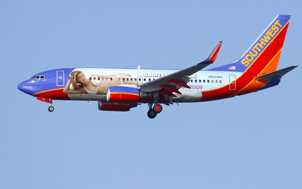 飛機 桌布 壁紙 — 一架西南航空波音737帶有大型女性廣告，在白天晴朗的藍天下飛行。