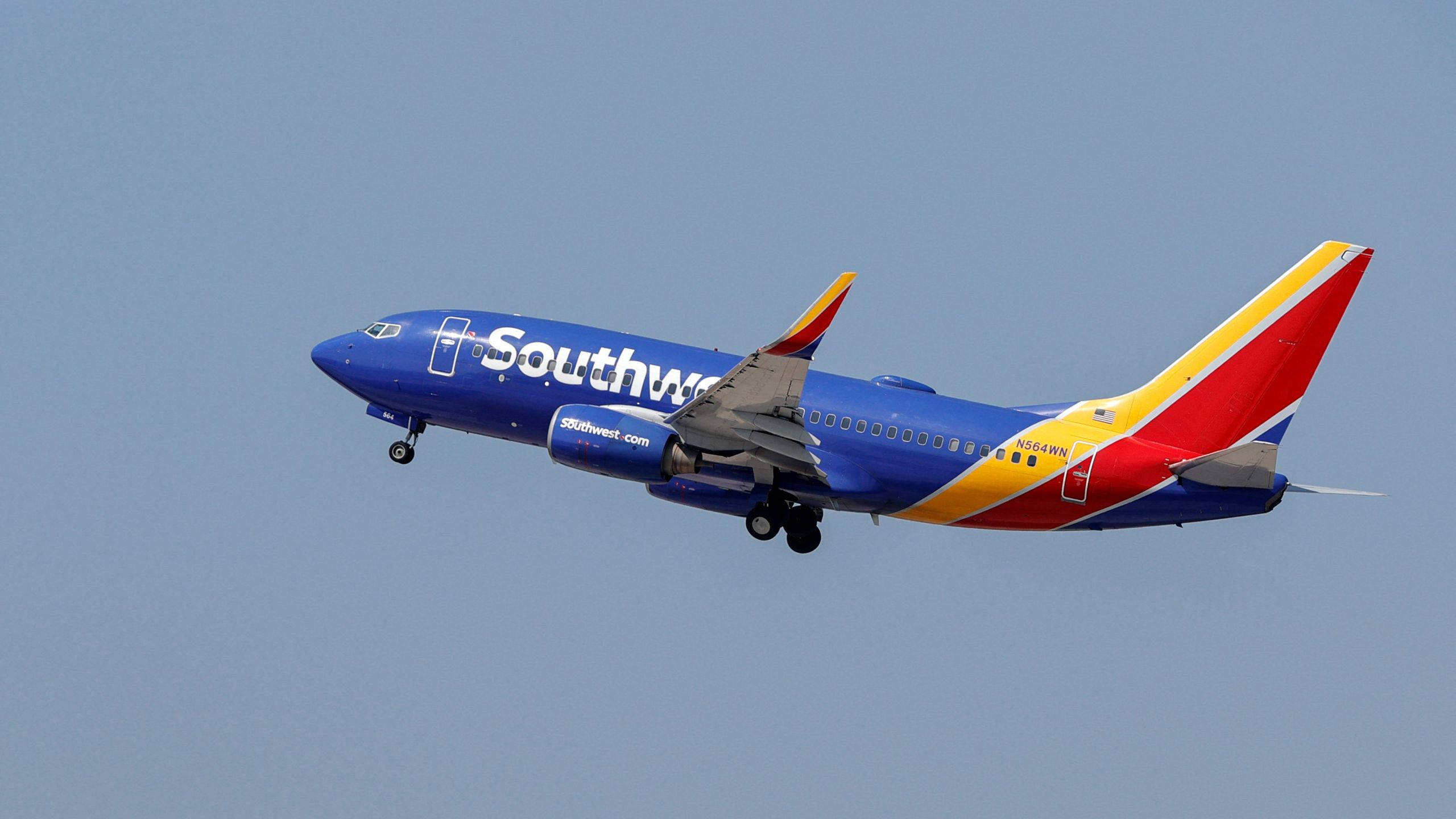 flying 桌布 壁紙 — 一架西南航空的波音737，以藍、紅、黃色塗裝，優雅地傾斜在清澈的淡藍色天空前。